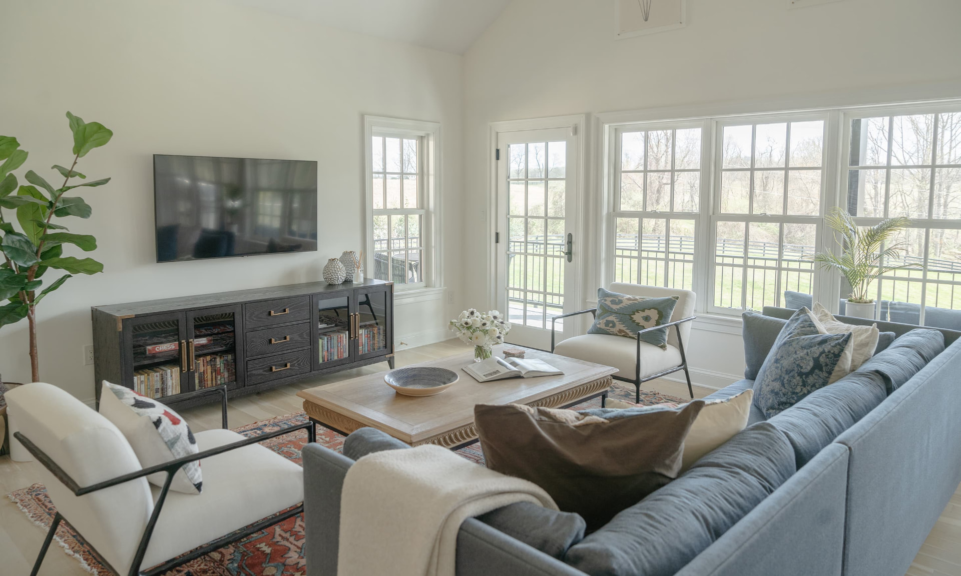 A bright guest-house living room with blue seating and windows overlooking fenced pastures