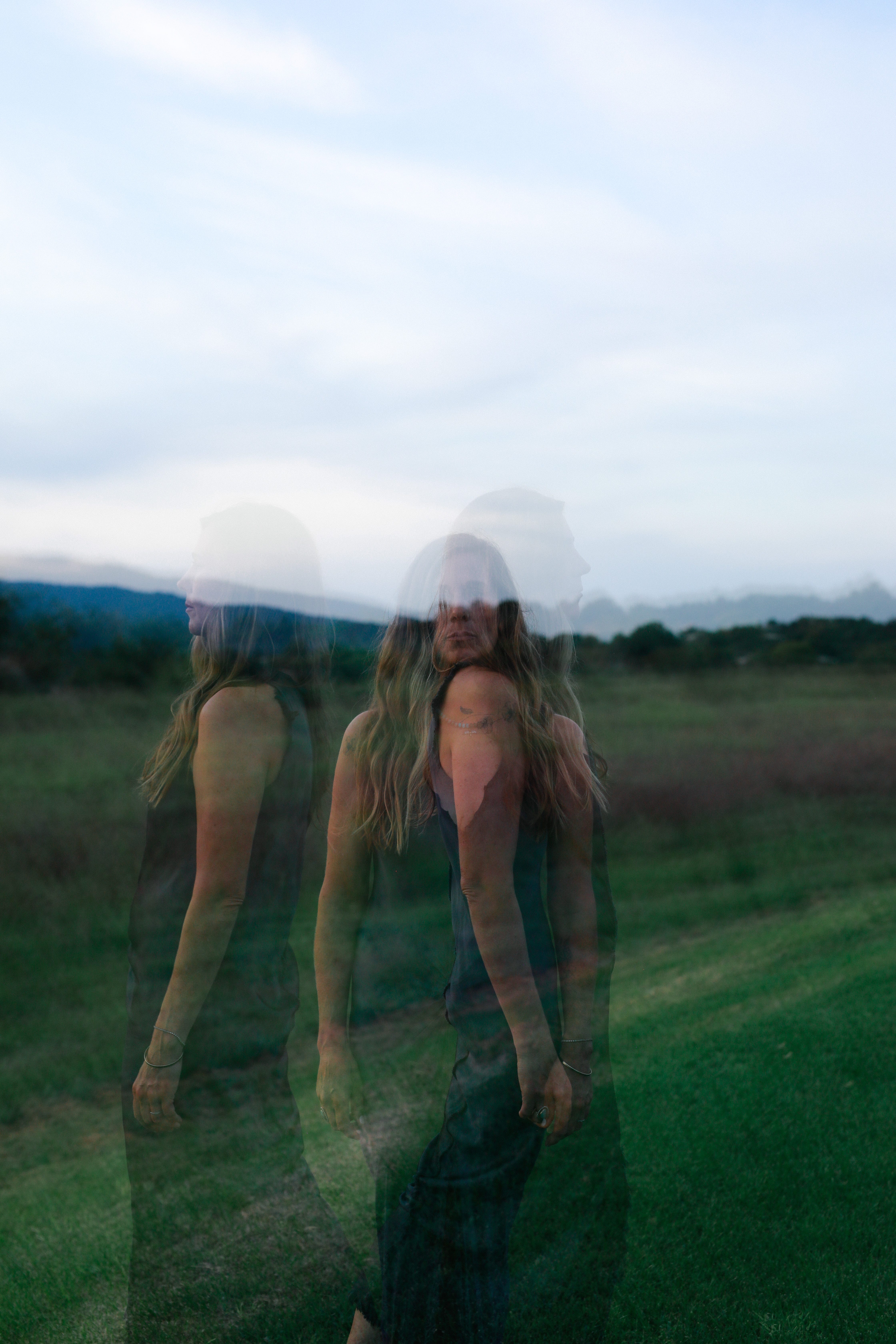 A layered portrait of Lindsay standing in a green field beneath an open sky