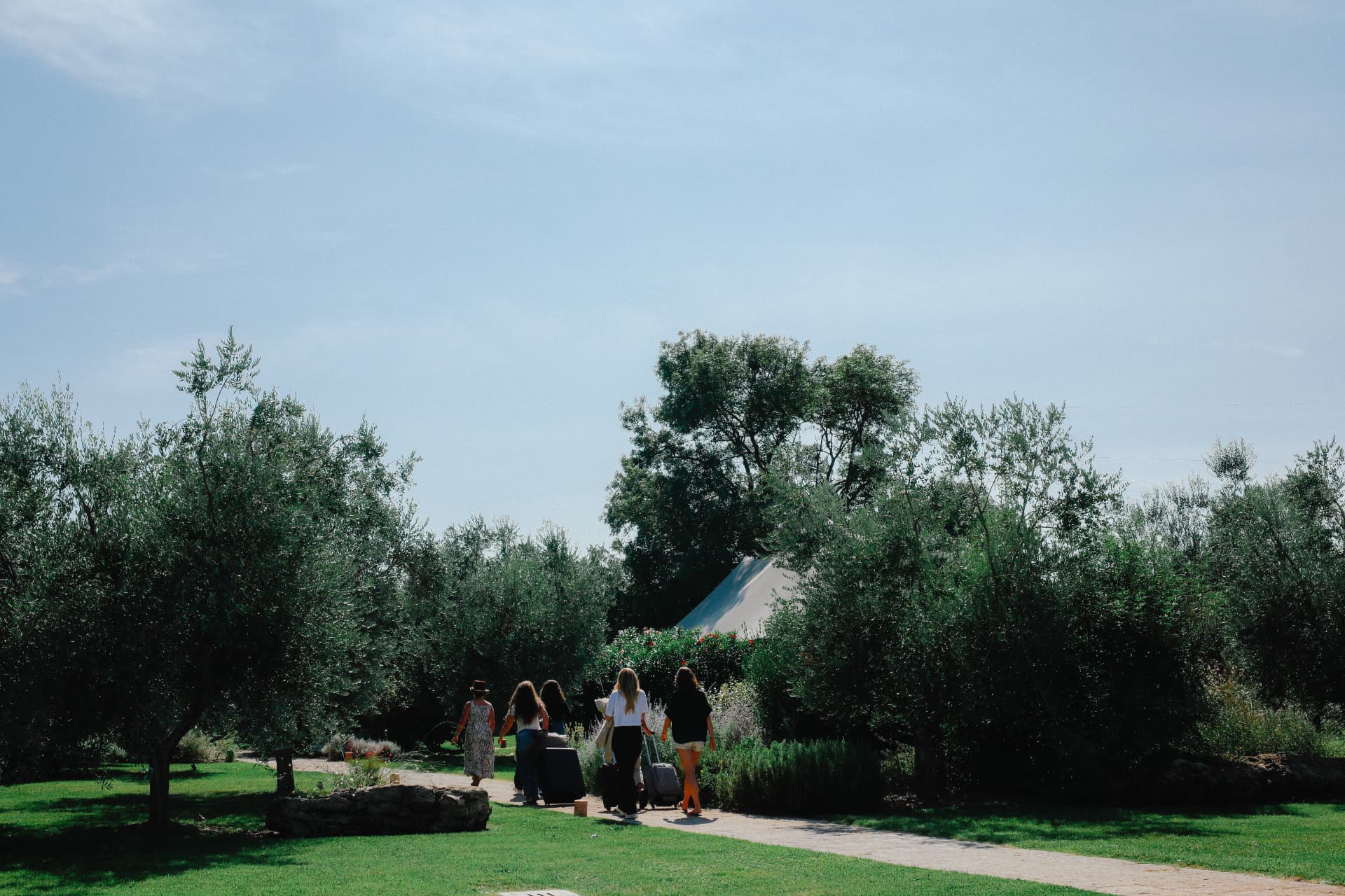Women arriving with their luggage along a garden path beneath olive trees