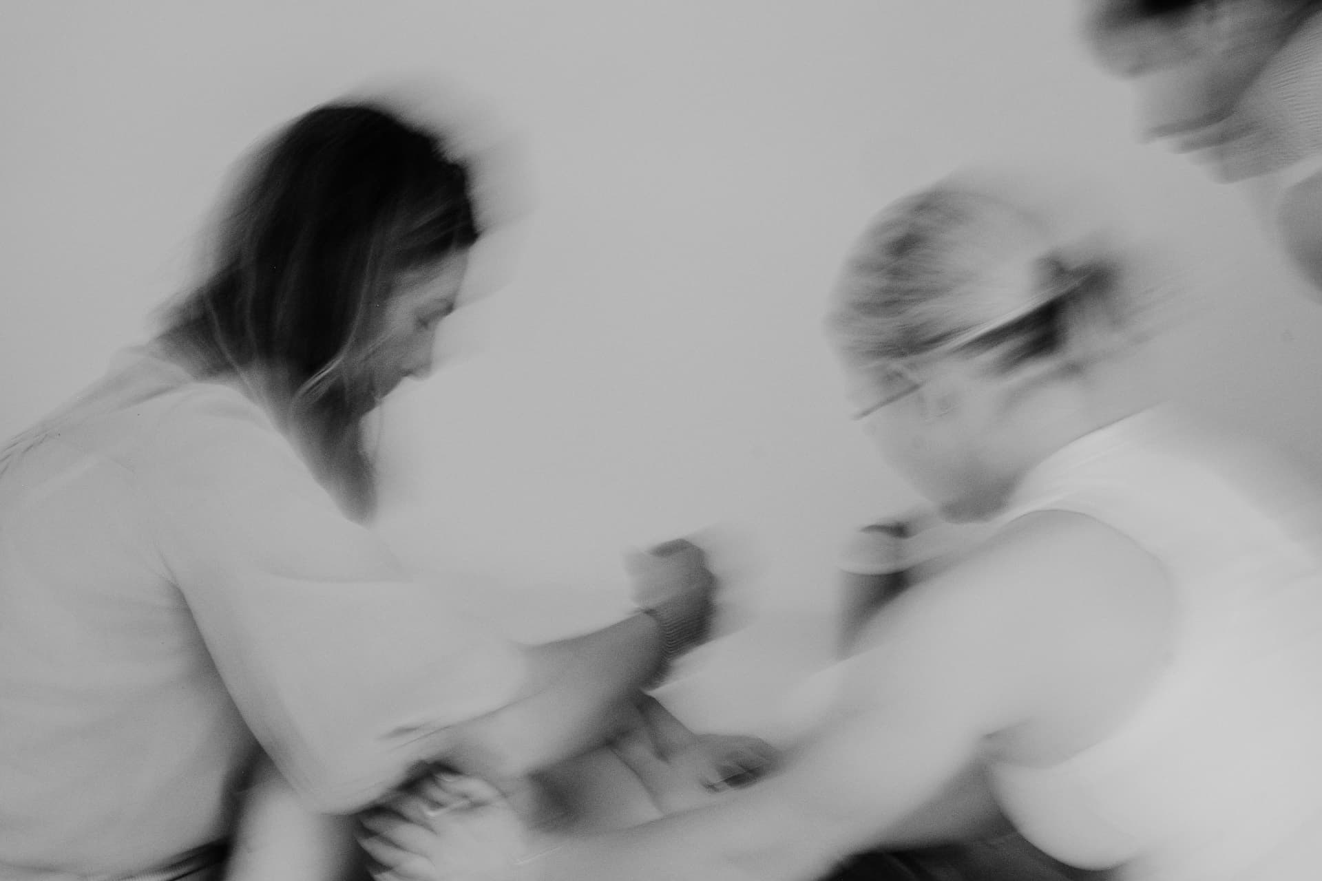 Women leaning in to care for one another, softly blurred in motion, in black and white