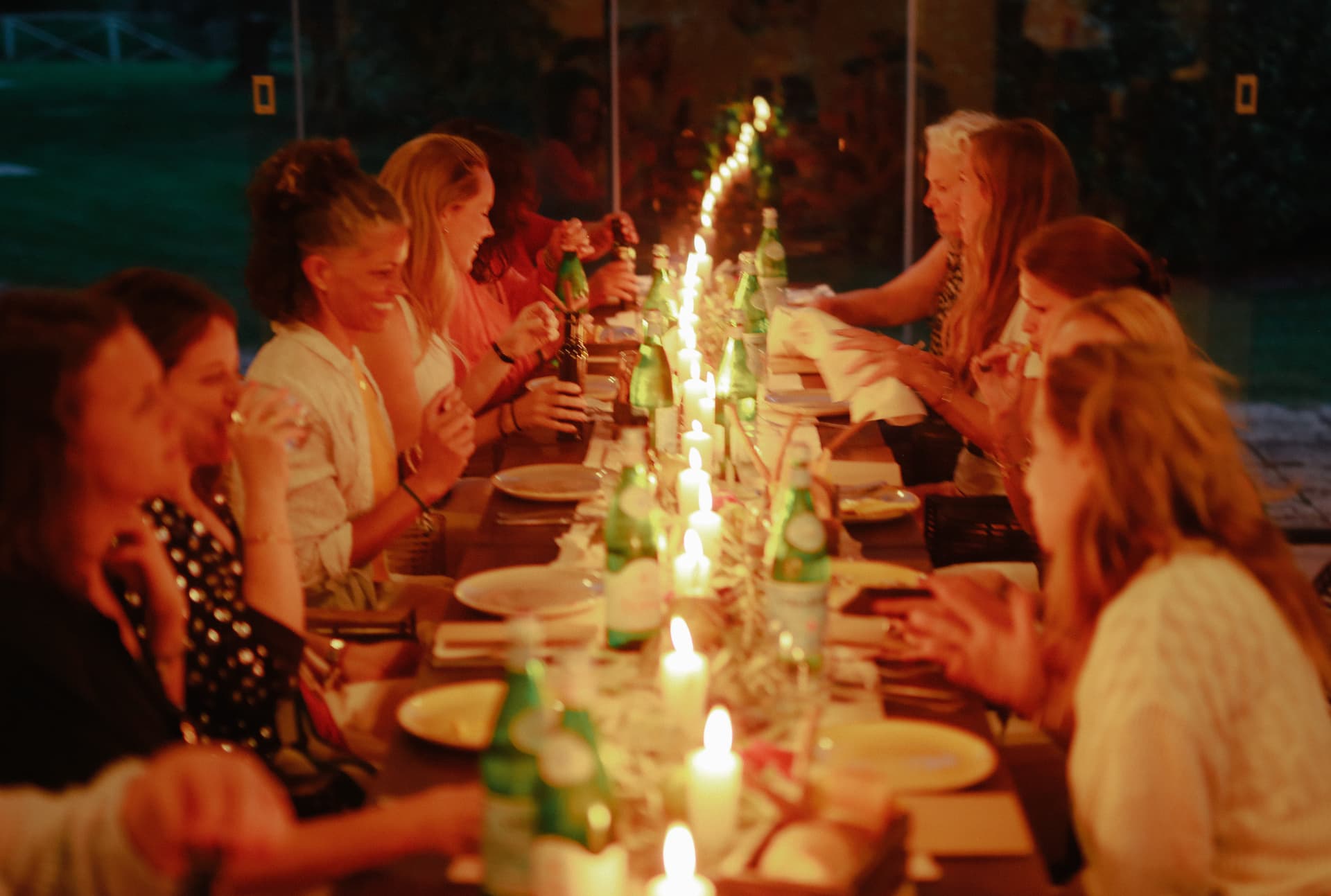 Women sharing dinner along a candlelit table in Italy