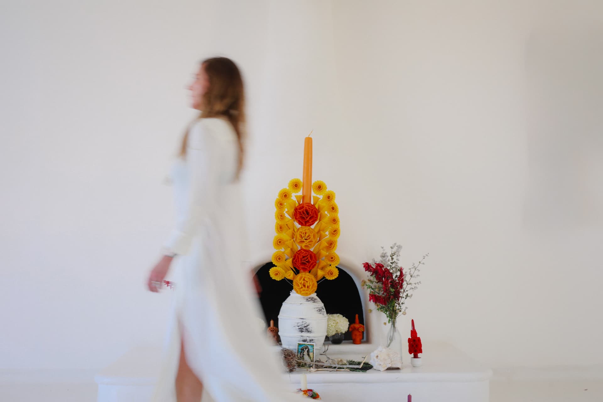 A woman in white walking past a marigold altar