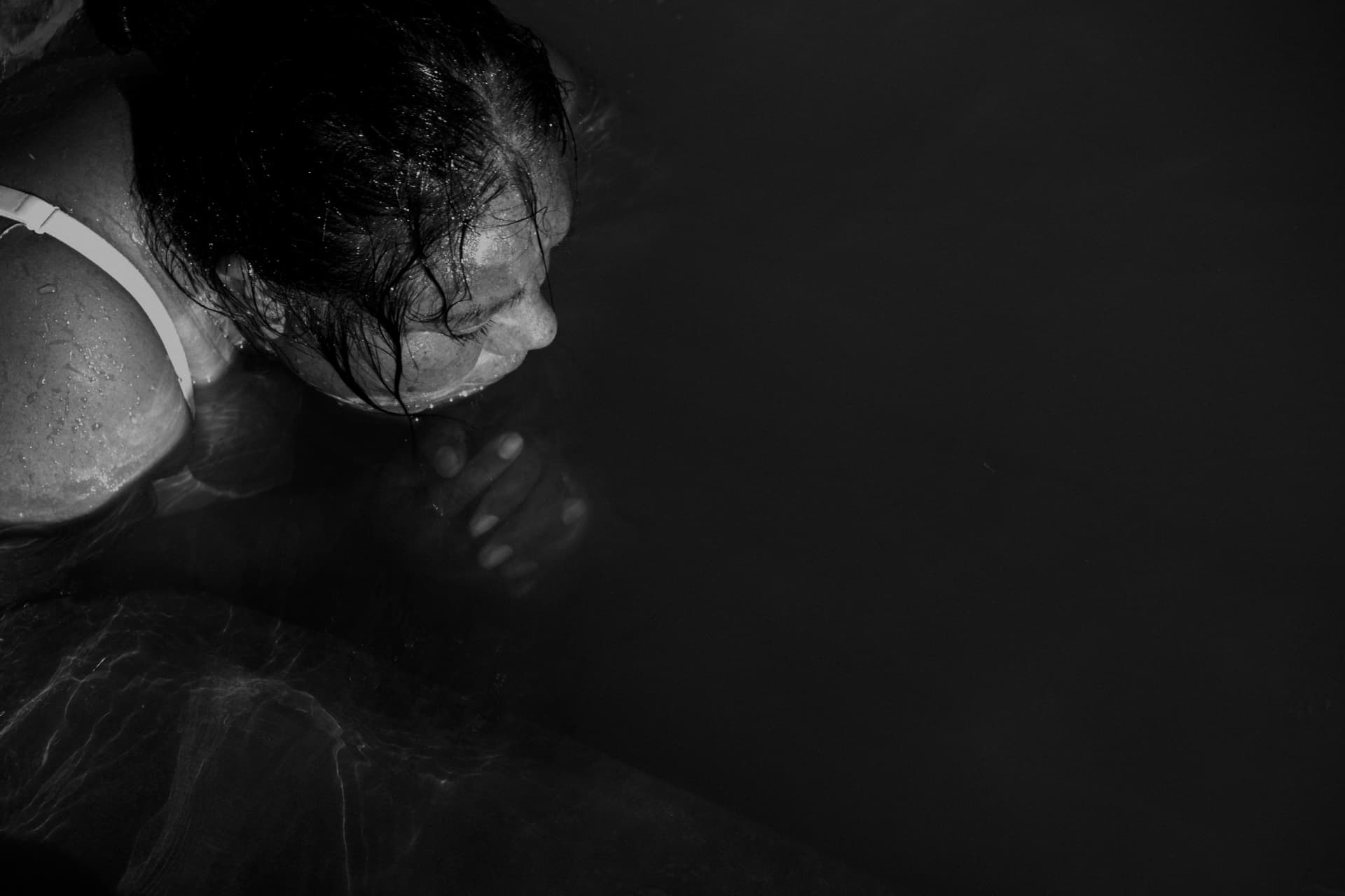 A woman bending forward in deep shadow, in black and white
