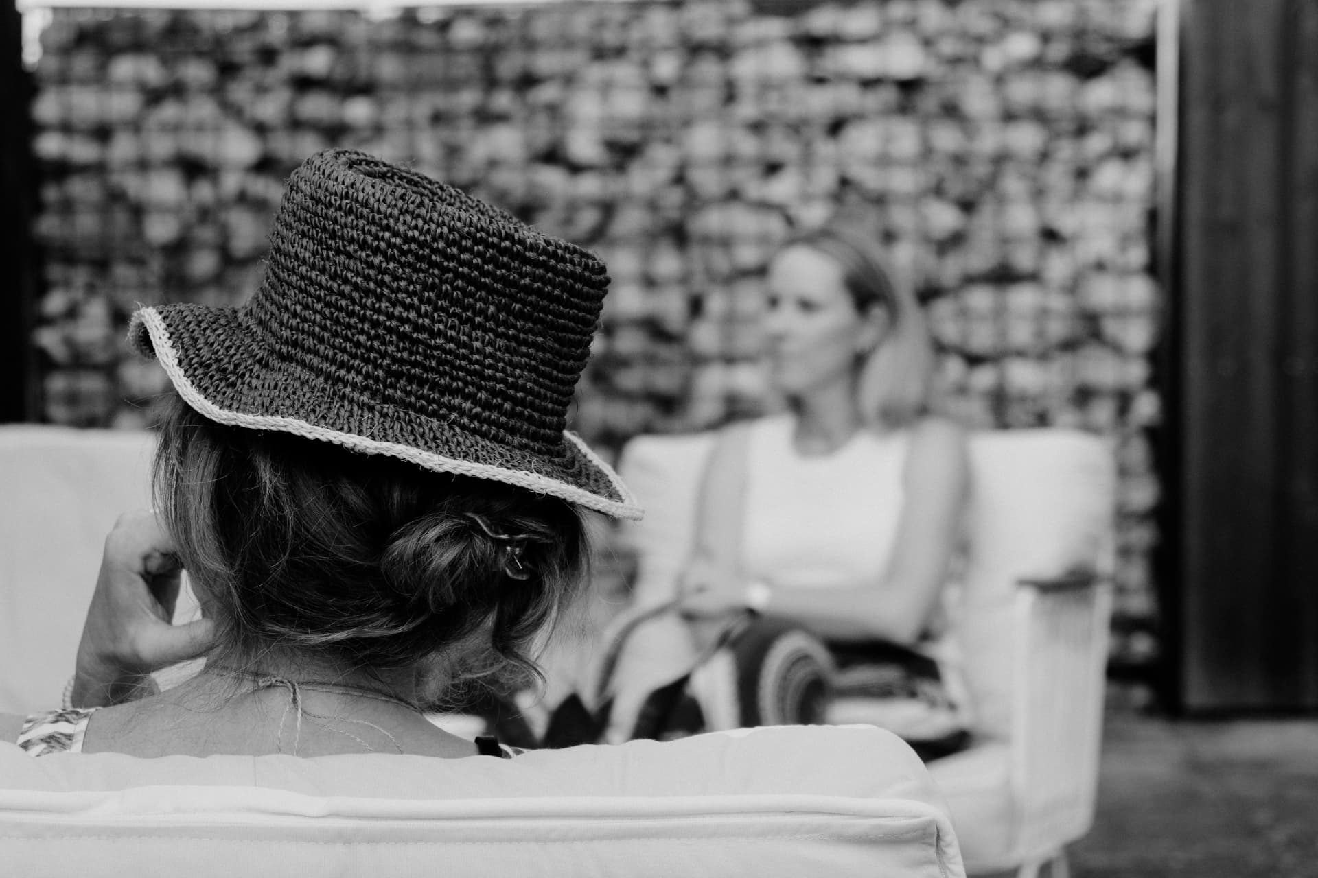 Black-and-white photograph of two seated women in conversation, with a woven hat in the foreground