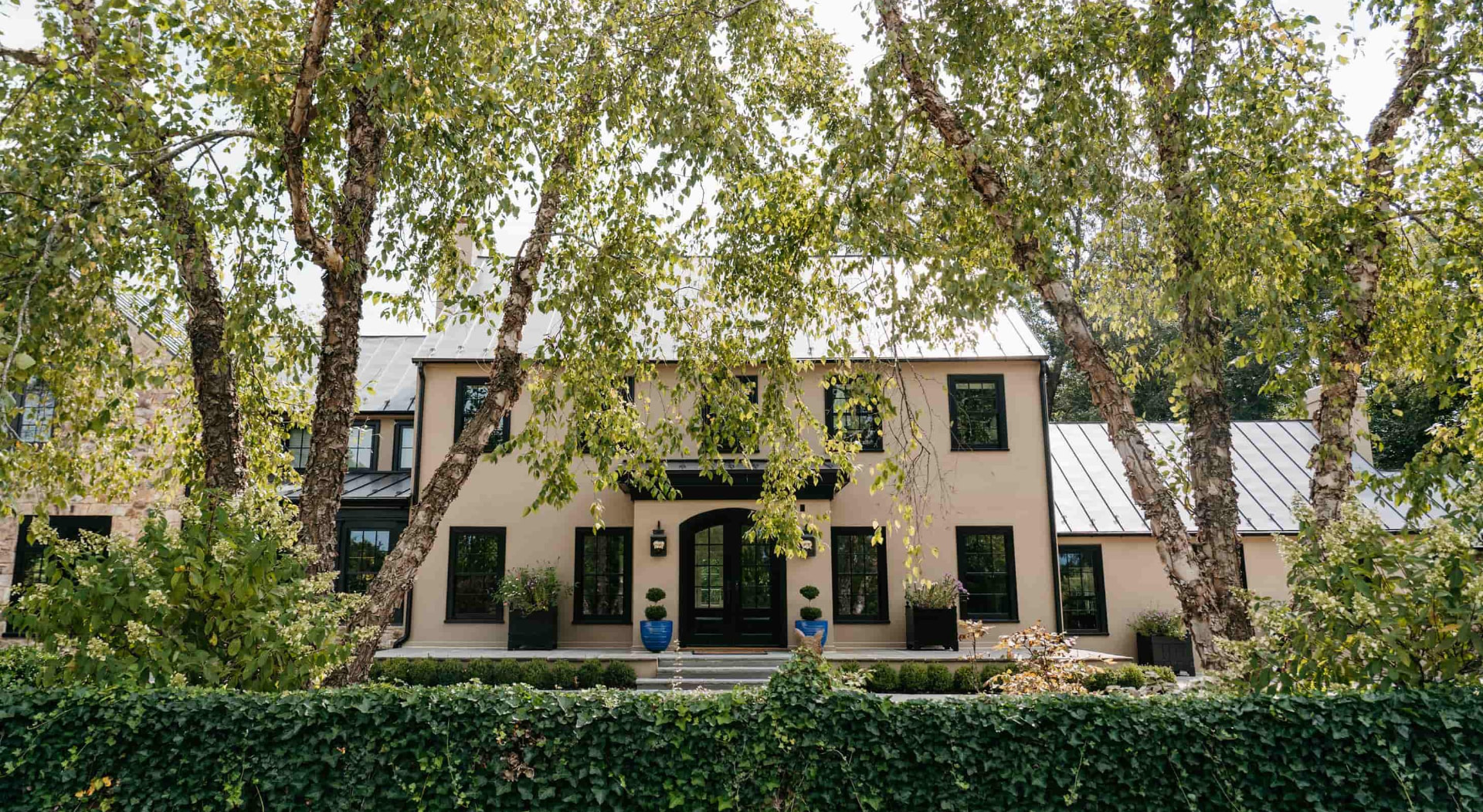 The farmhouse framed by leafy birch trees, with blue pots beside the entrance