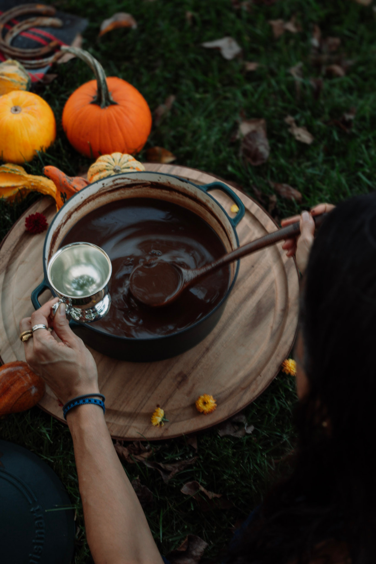 Hands stirring a pot of cacao beside pumpkins, gourds and autumn flowers