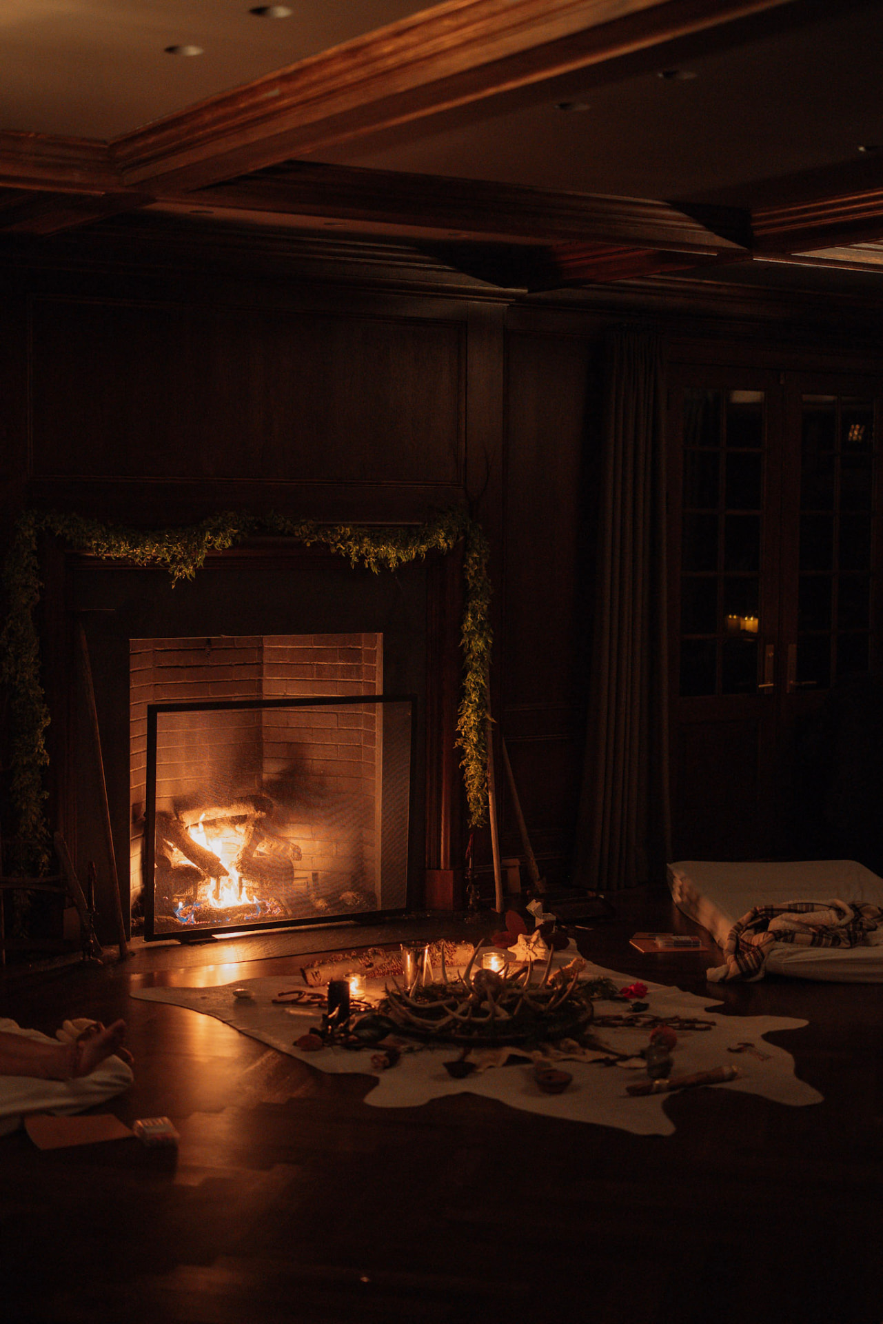 An antler altar laid with candles before a glowing fire in a wood panelled room