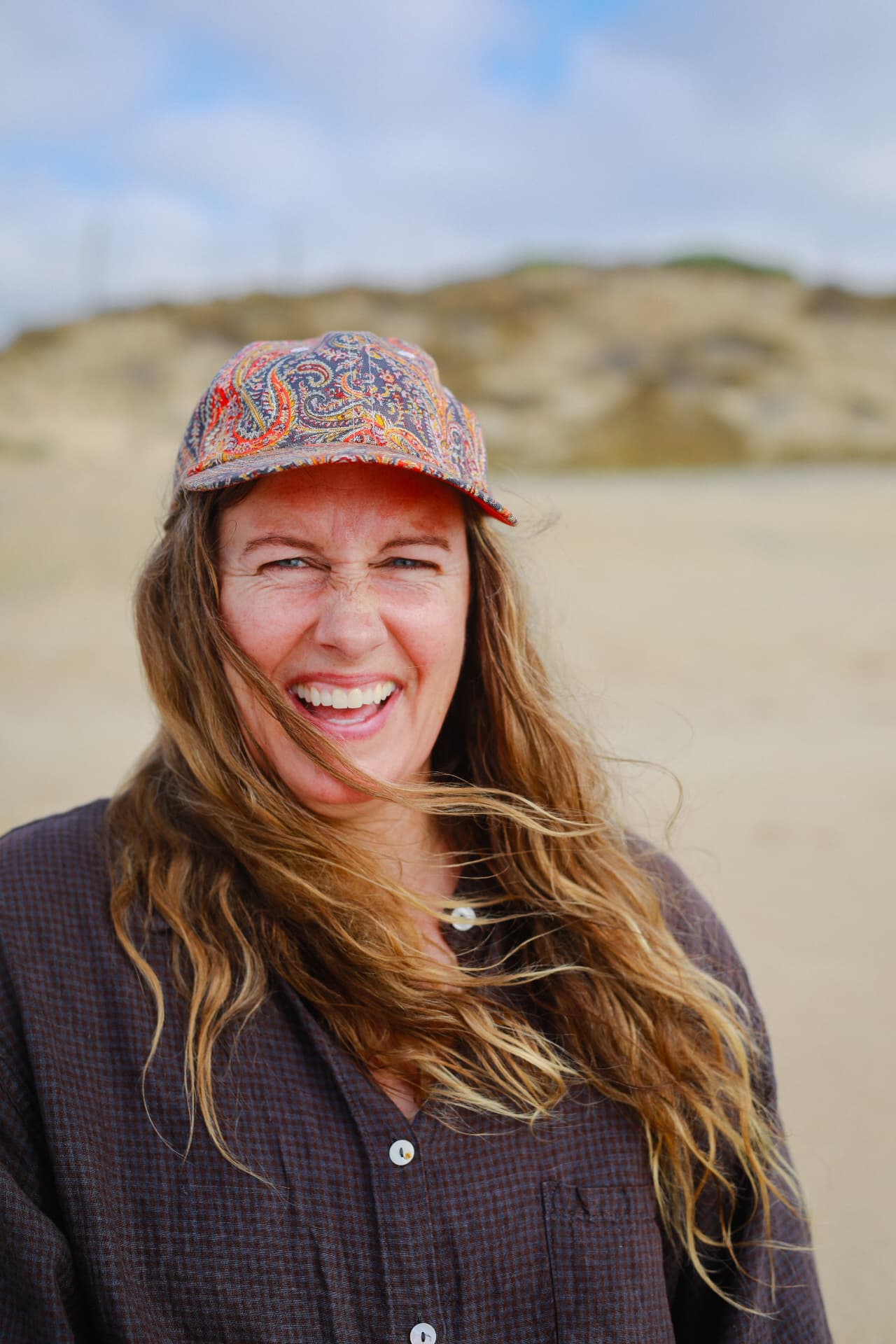 A woman laughing on the beach in a colorful patterned cap