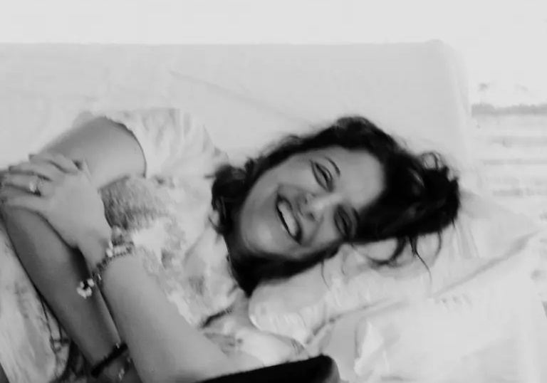 A woman laughing as she rests on white bedding, in black and white