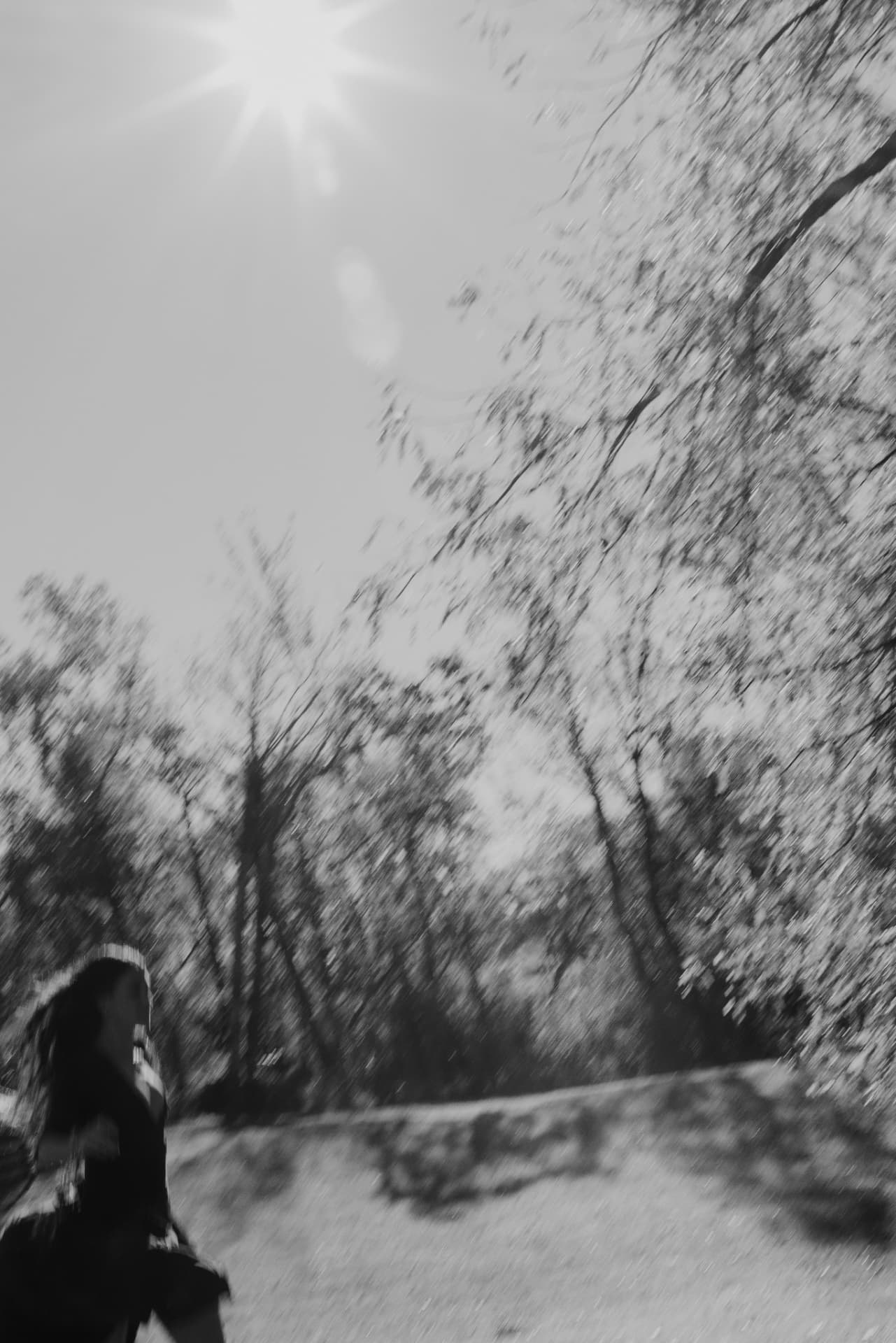 A woman running beneath sunlit, wind-blurred trees, in black and white