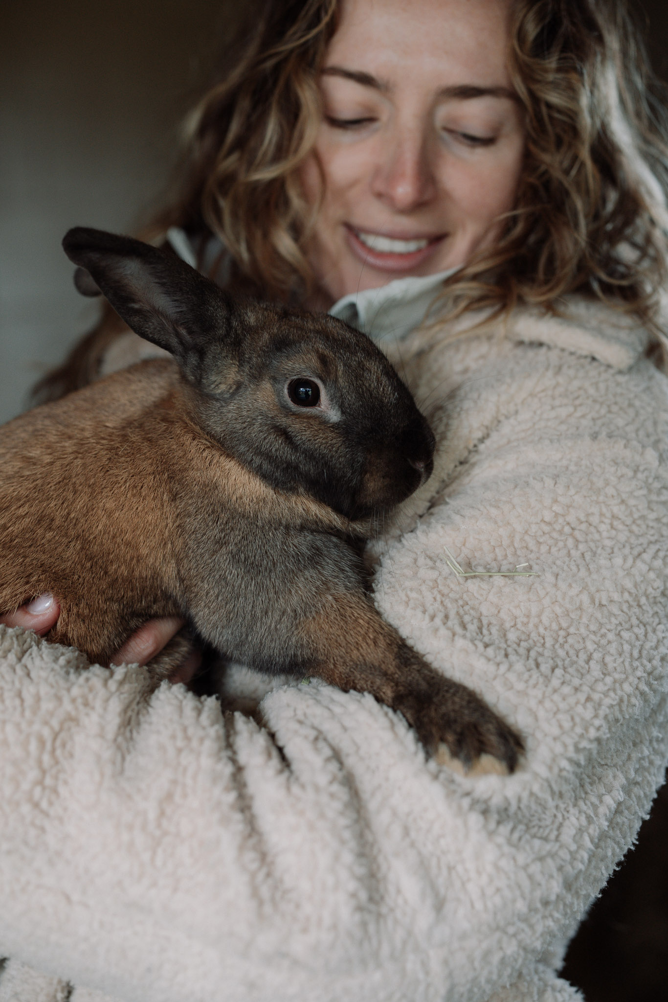 A smiling woman holding a rabbit close against her sweater