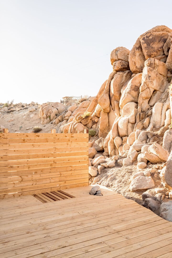 An outdoor shower on a wooden deck beside towering desert boulders
