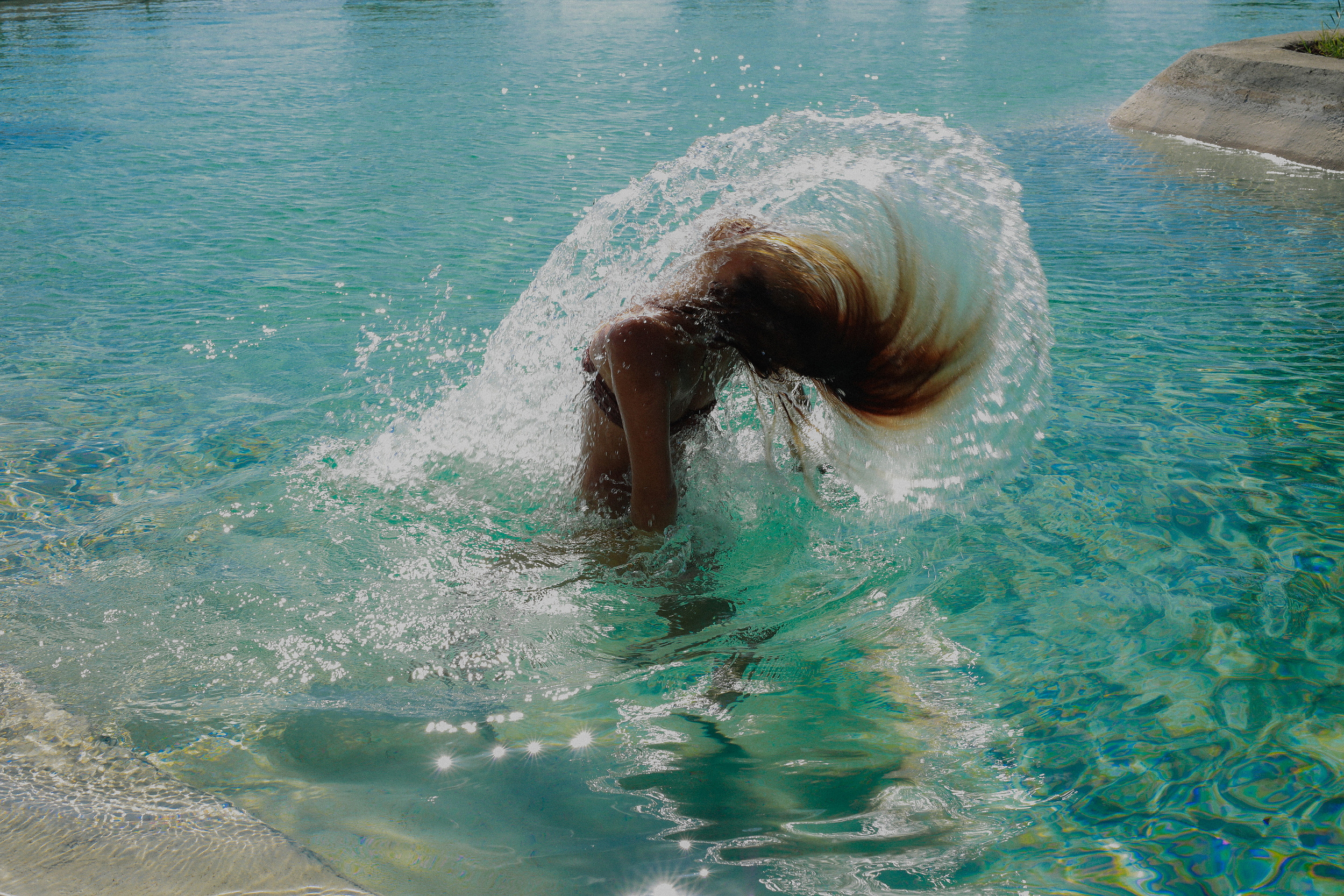 A woman flipping her wet hair up from turquoise water