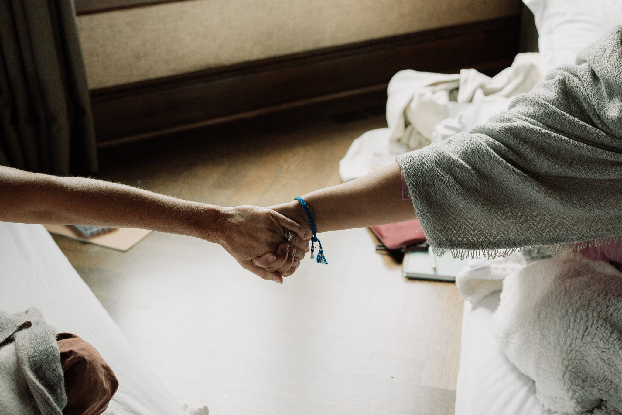 Two women holding hands between softly draped blankets in window light at a FADEN gathering