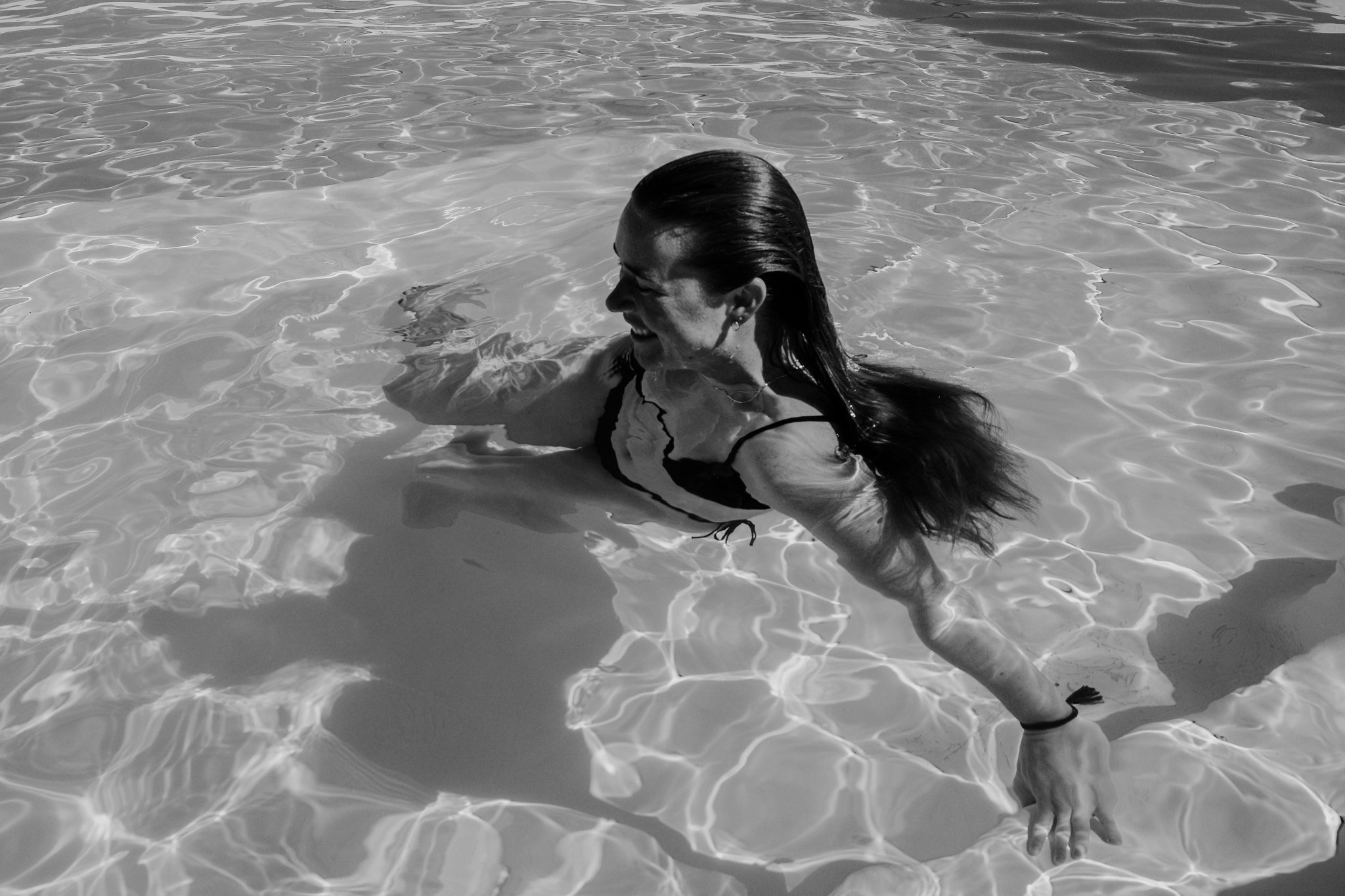 A woman resting in rippling pool water, in black and white