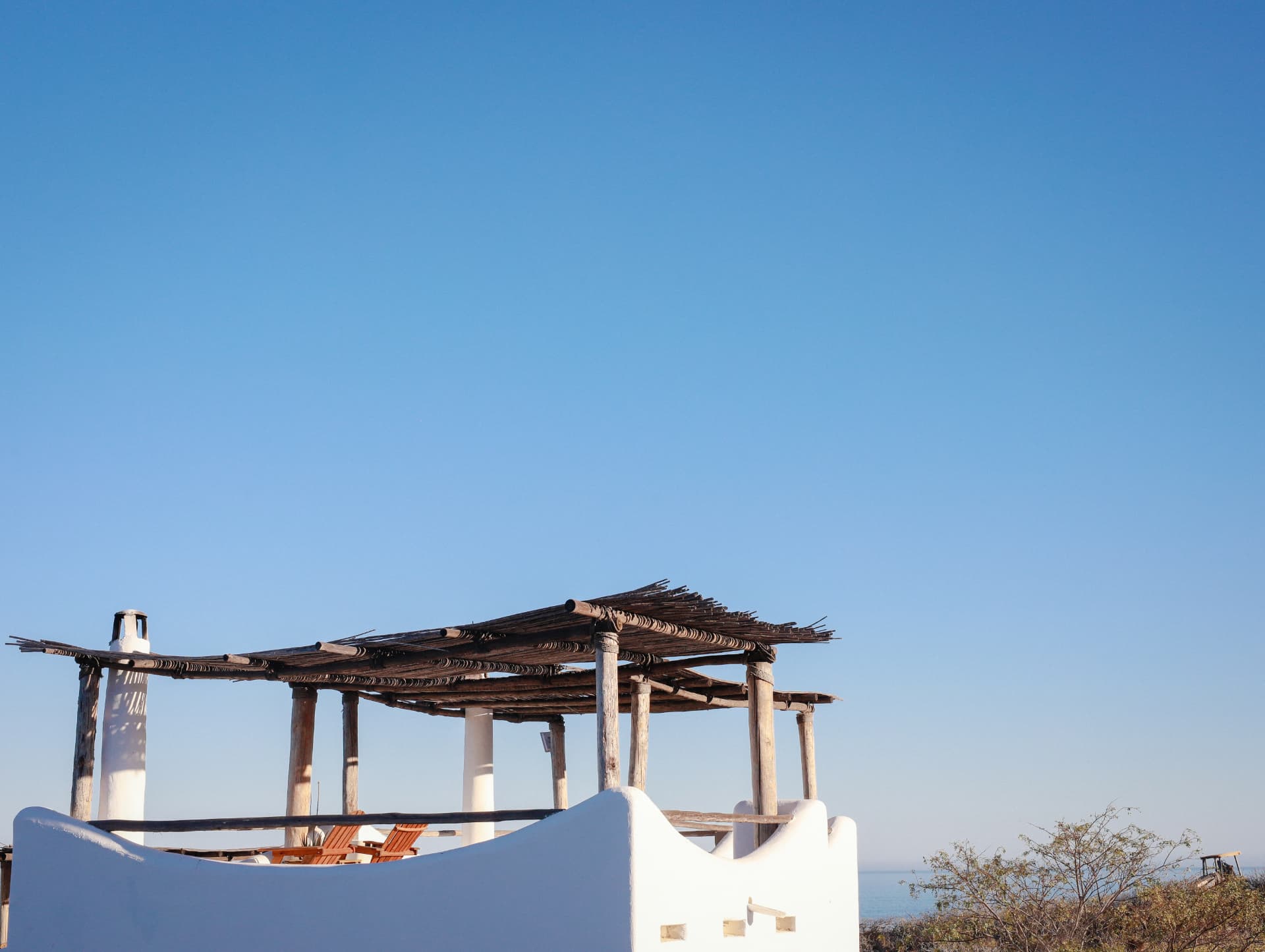 An open rooftop shaded by a rustic wooden pergola beneath a blue sky