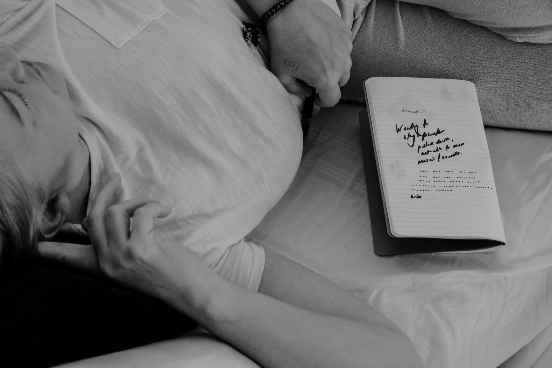A woman resting with eyes closed beside an open handwritten journal, in black and white