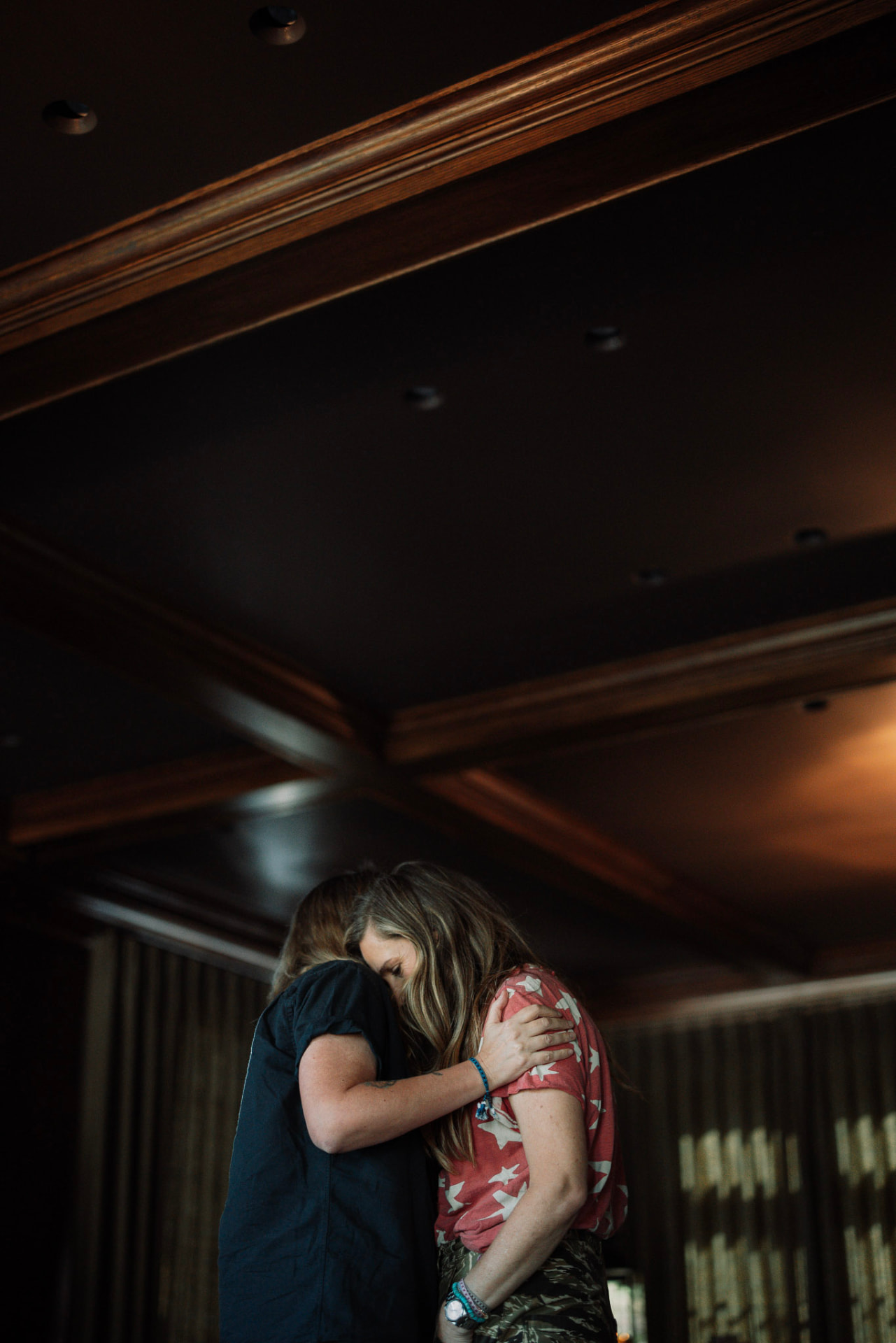 Two women sharing an embrace beneath the dark wooden ceiling