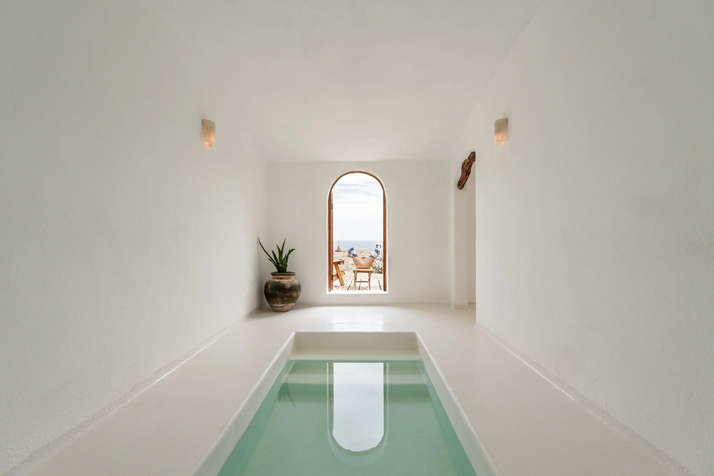 A narrow indoor plunge pool within white curved walls beneath an arched window