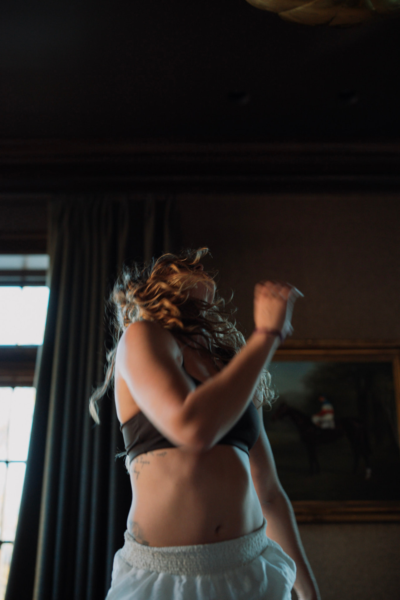 A woman dancing freely, her curls in motion, beneath a horse painting