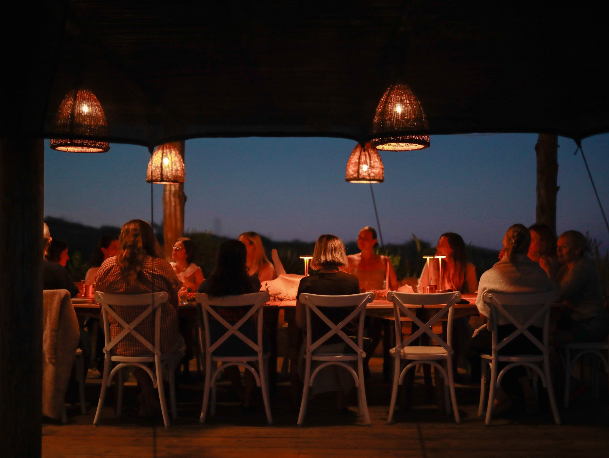 Women at a long table beneath lanterns at dusk