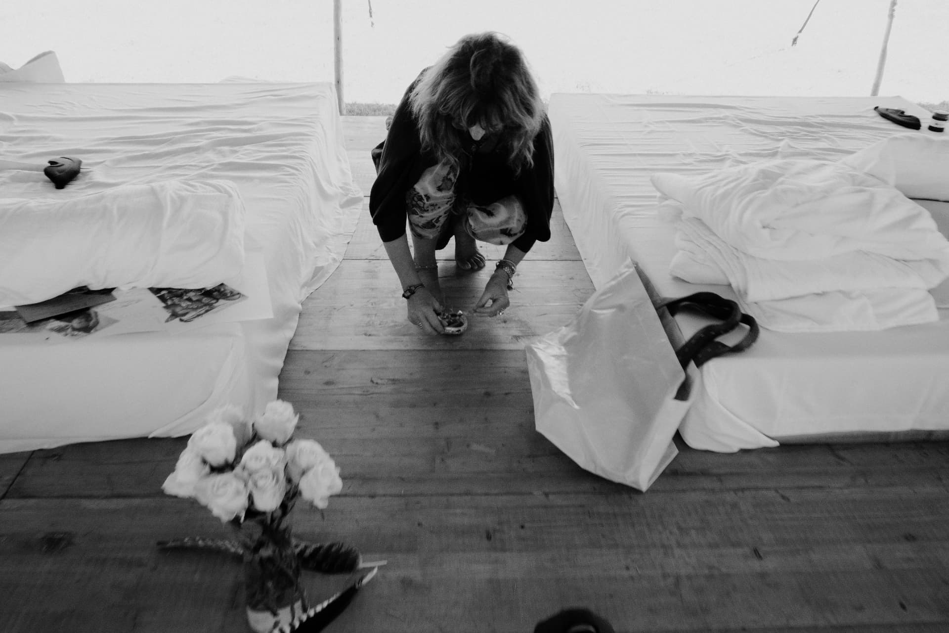 A woman kneeling between white mattresses beside gathered objects, in black and white