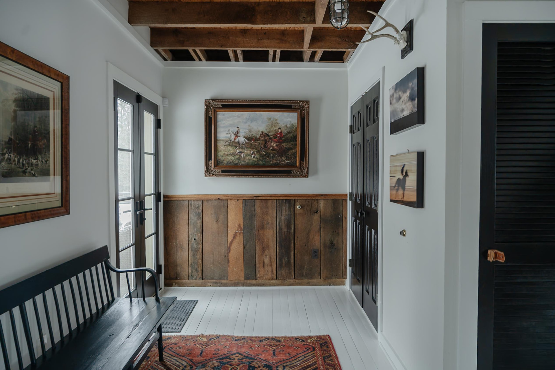 A cottage entry with exposed beams, equestrian artwork and a black wooden bench