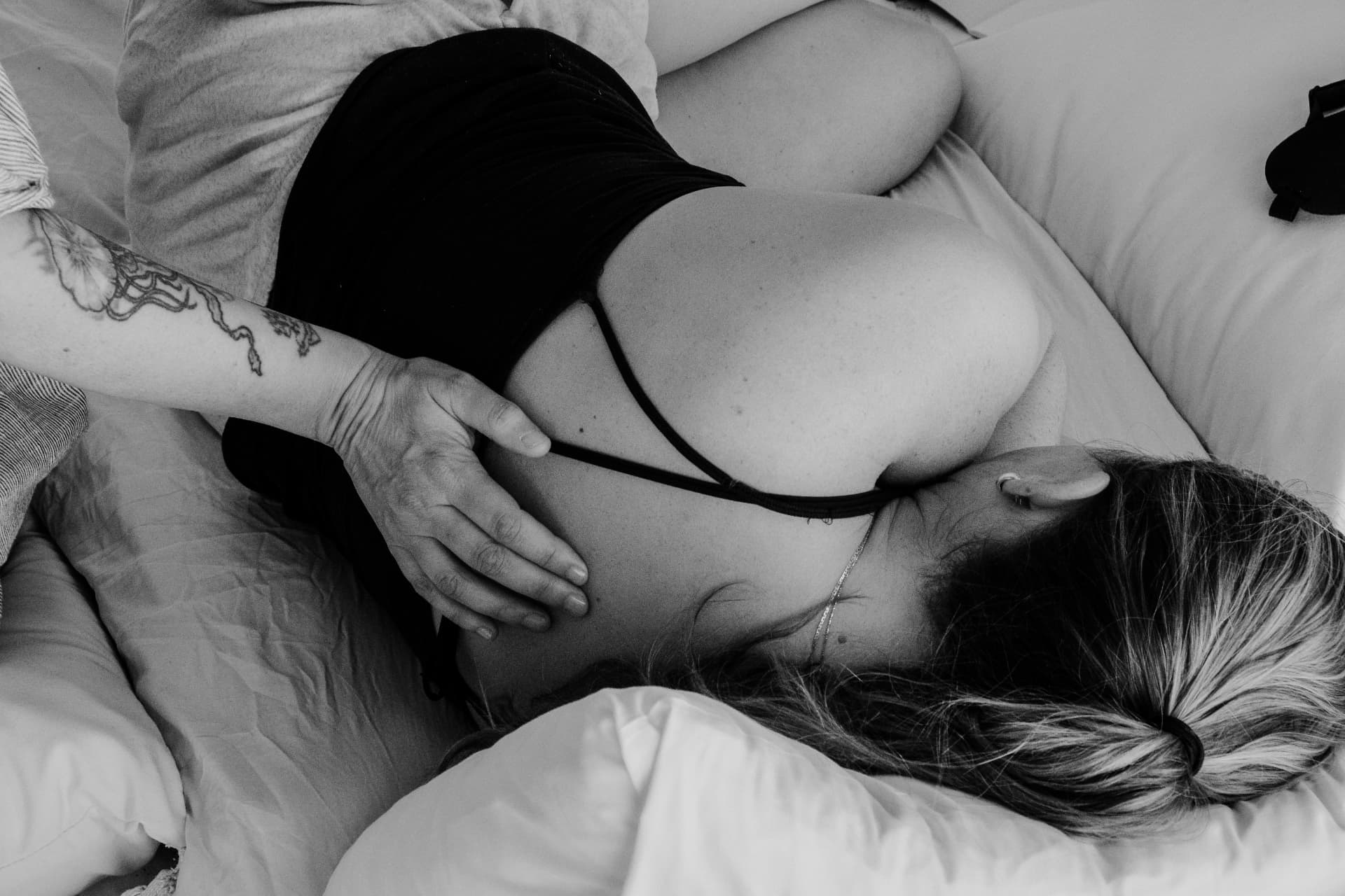 A woman resting on white cushions with a hand gently placed on her back, in black and white