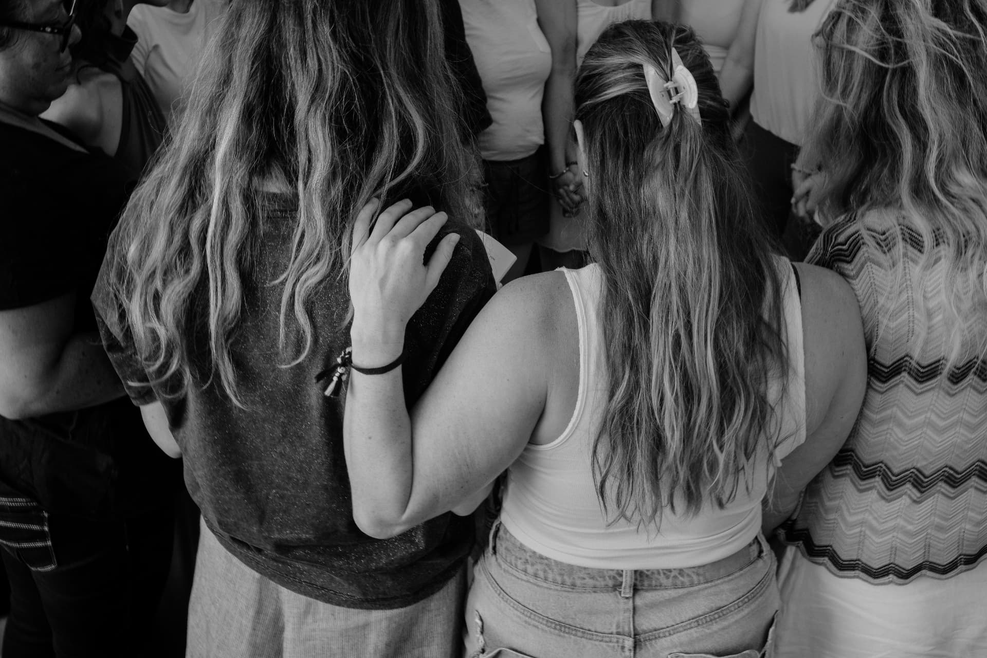 Women standing close together with their backs to the camera, in black and white