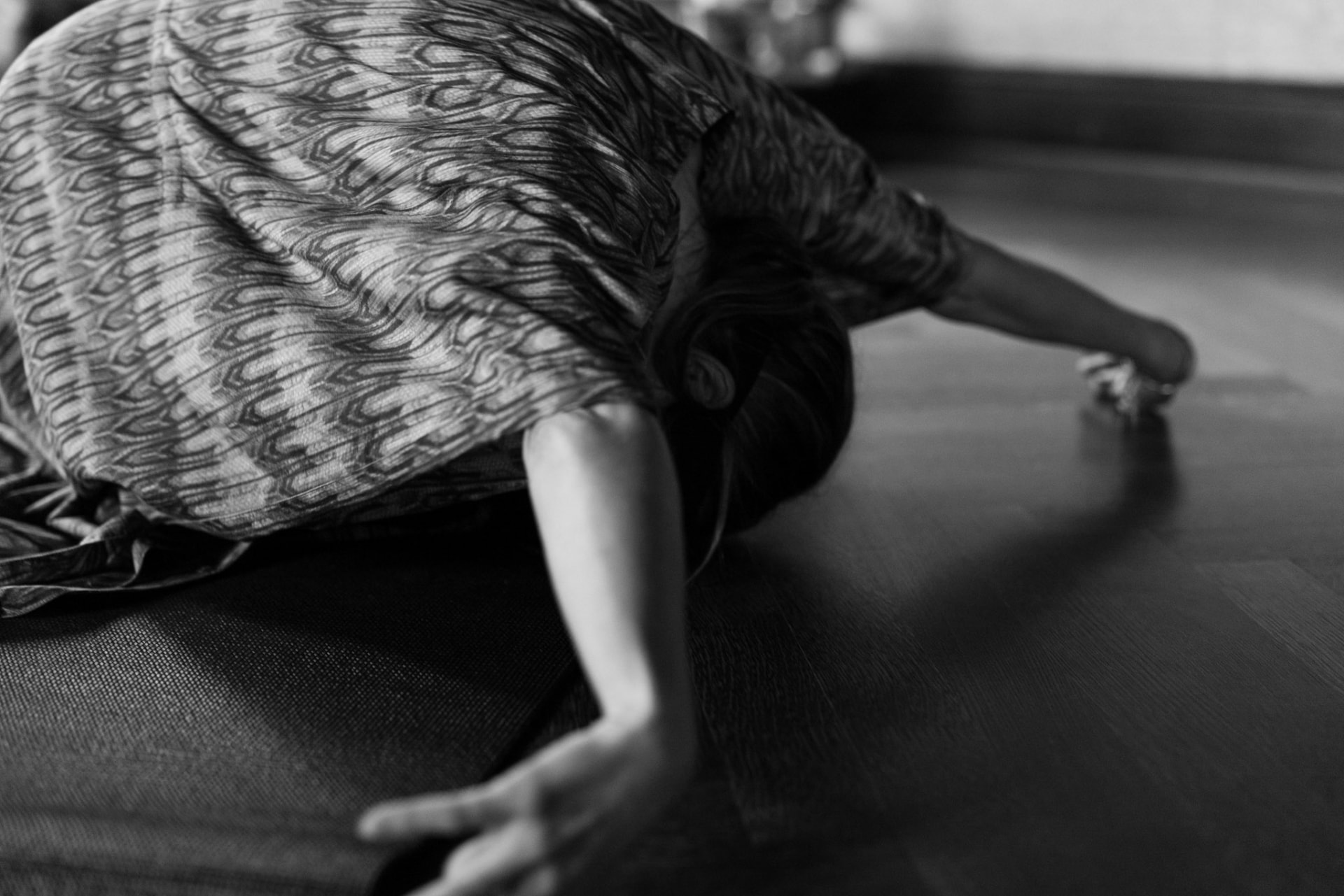 A woman crawling slowly across the floor in a patterned dress, in black and white