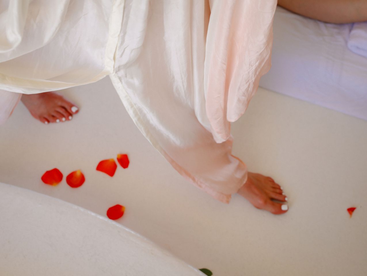 Bare feet stepping among vivid rose petals, pale fabric falling softly around them