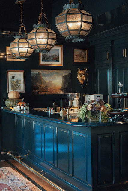 A deep blue farmhouse kitchen with woven pendant lamps and flowers on the island