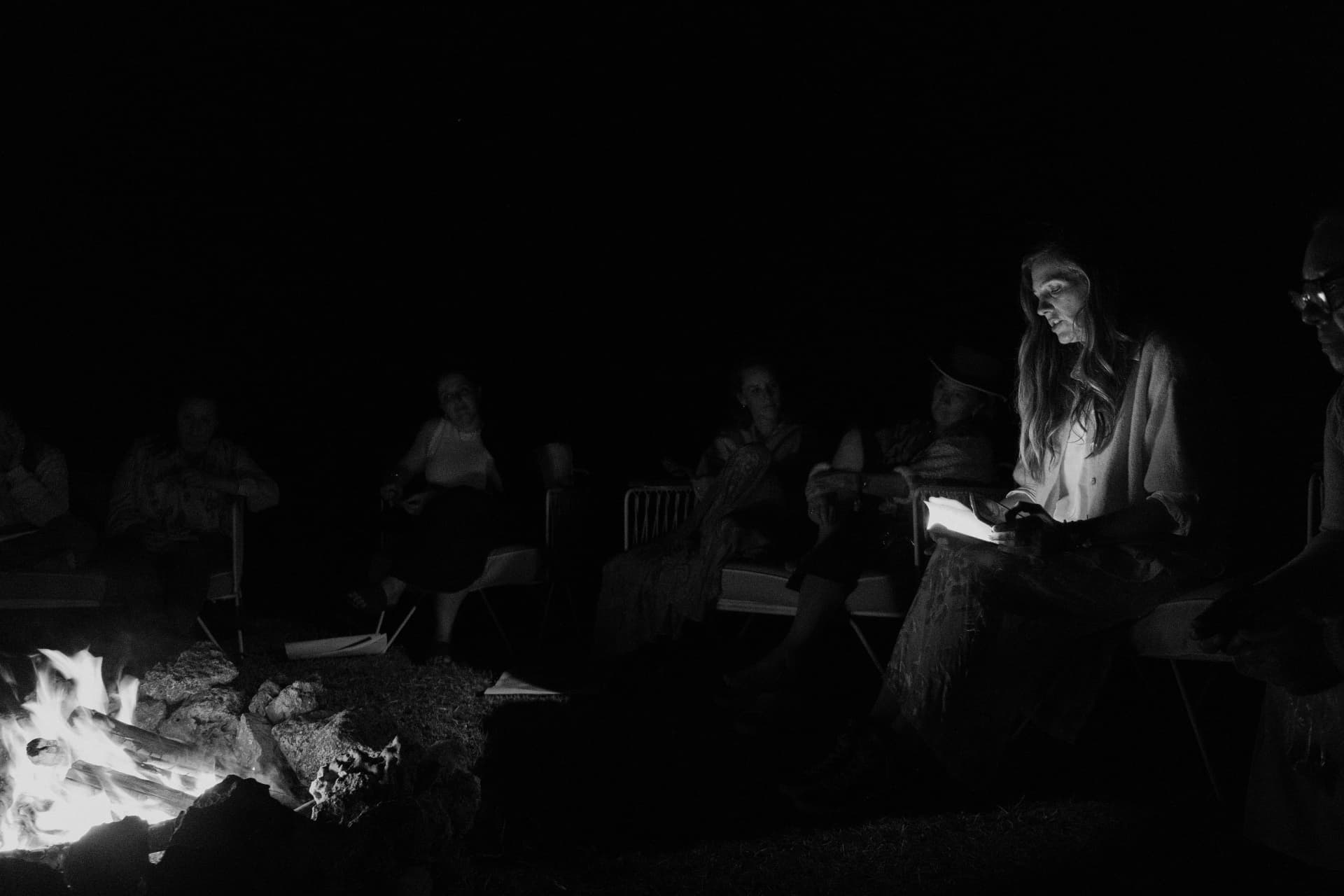 Women gathered in darkness beside a fire at night, in black and white