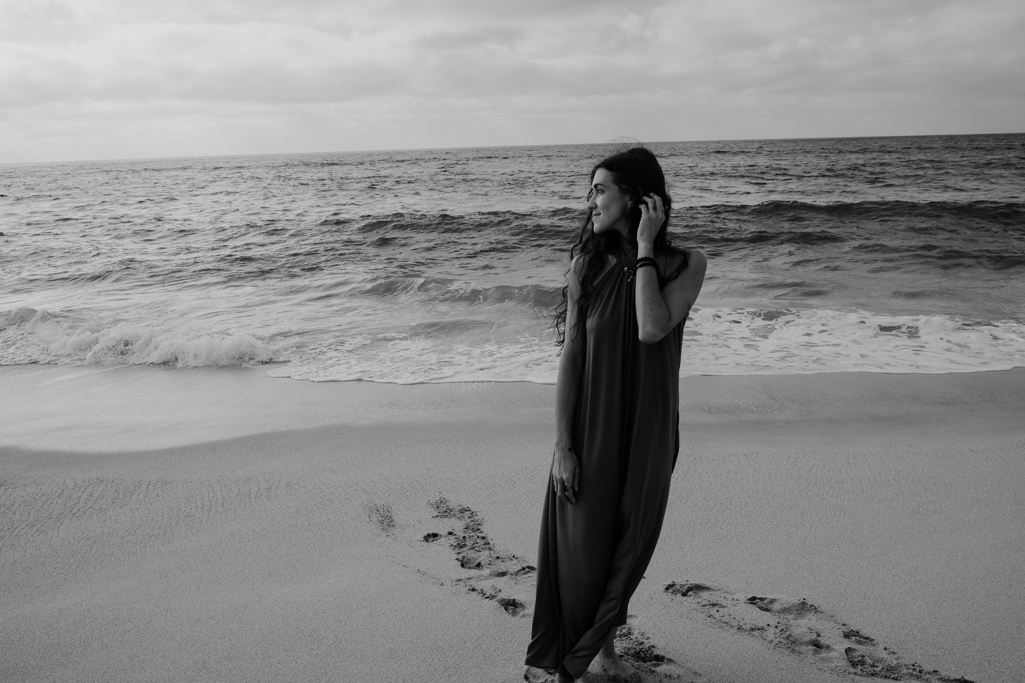 A woman standing alone on the shore with footprints in the sand, in black and white
