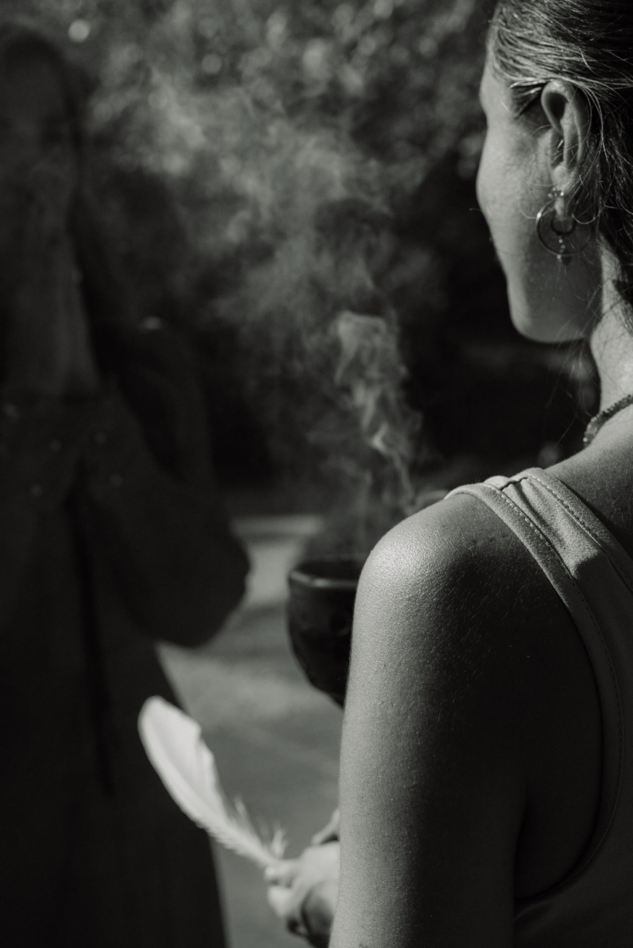 Smoke rising beside a woman holding a feather, in black and white