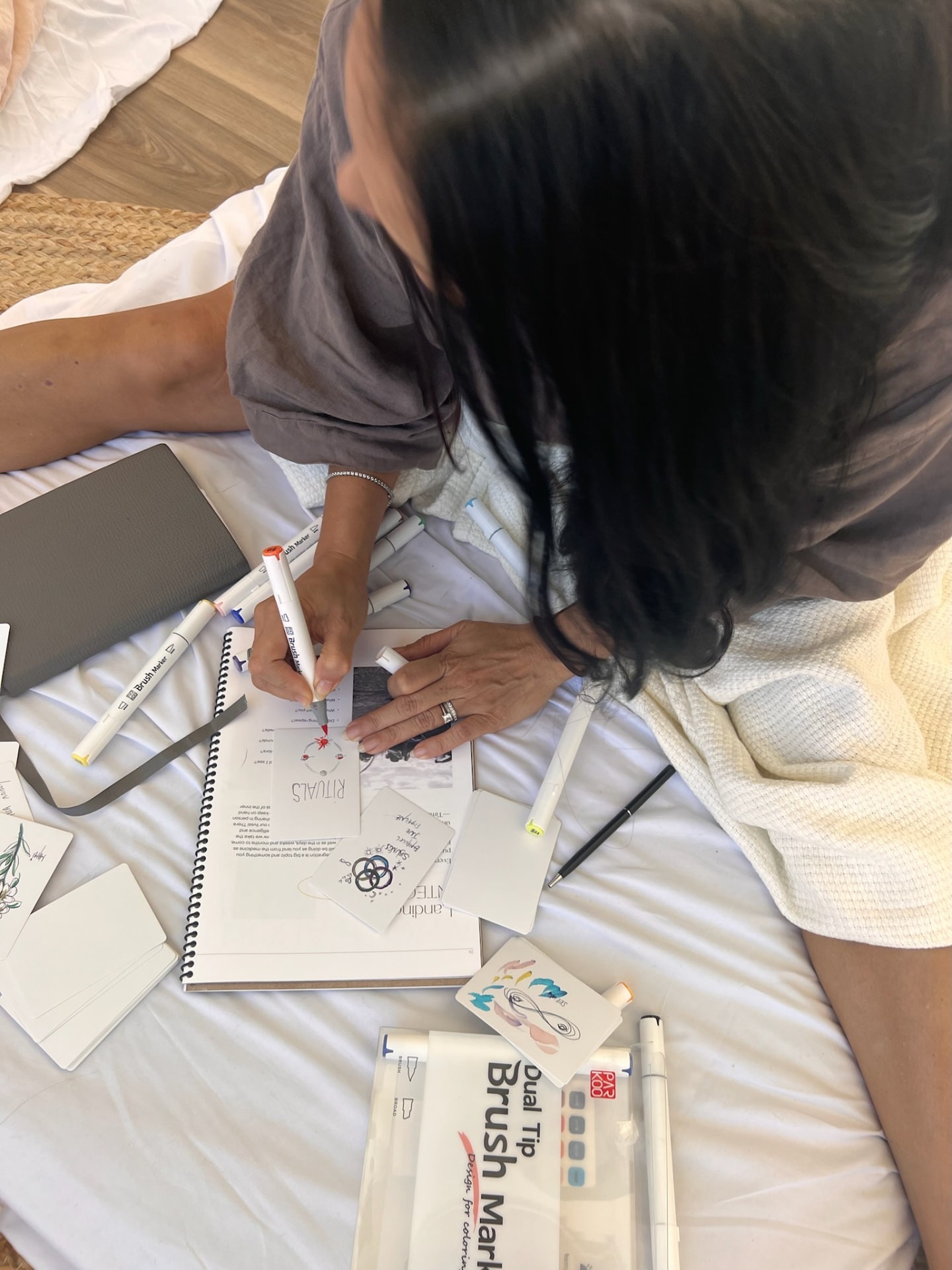 A woman drawing a flower in a notebook beside watercolor materials