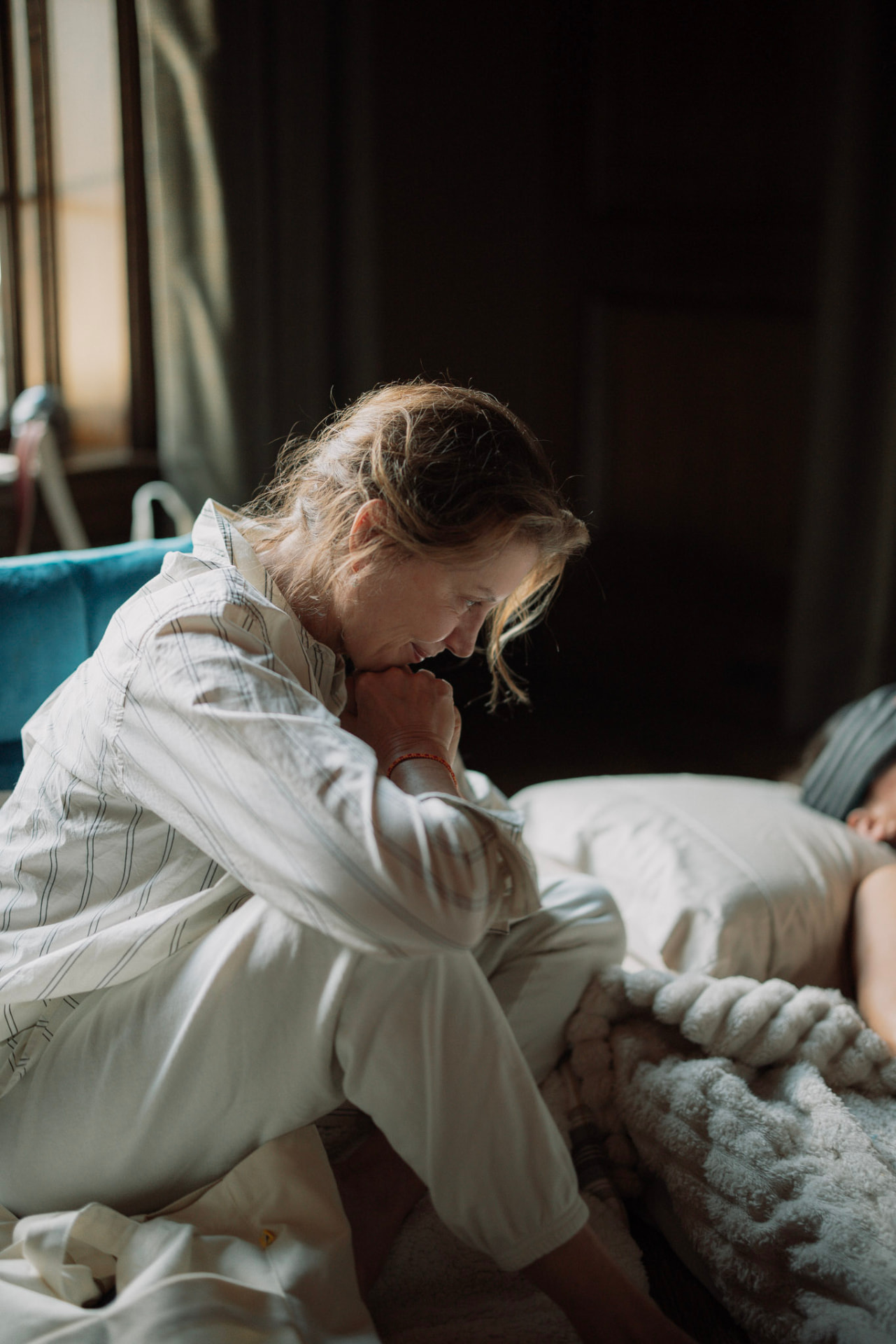 A woman sitting attentively beside another woman resting beneath a blanket
