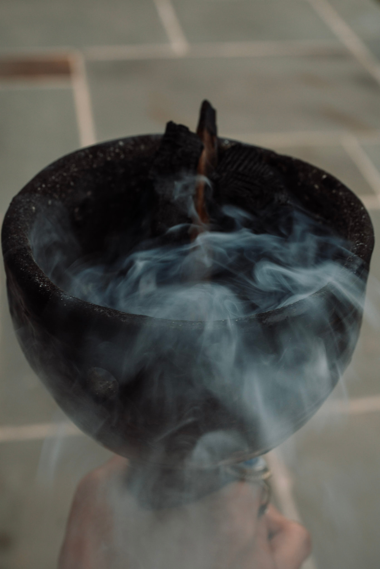 Smoke curling from a dark ritual bowl held in a hand