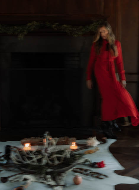 Lindsay in a red dress beside the hearth and gathered objects