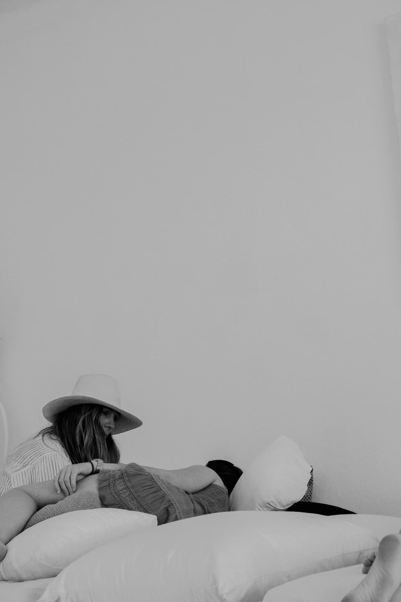 A woman in a hat resting against white cushions, in black and white