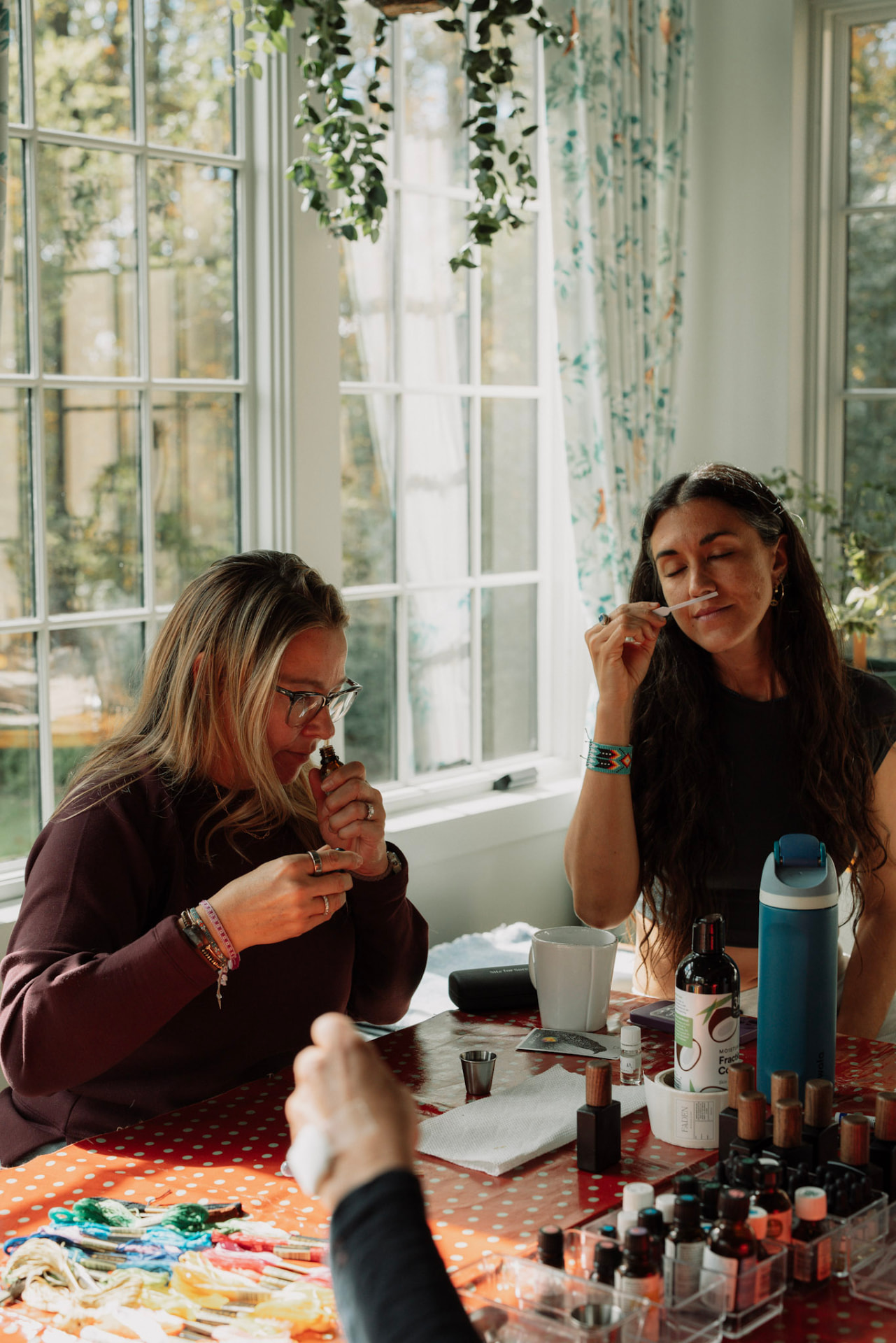Women exploring perfumes at a sunlit table with scent strips and small bottles