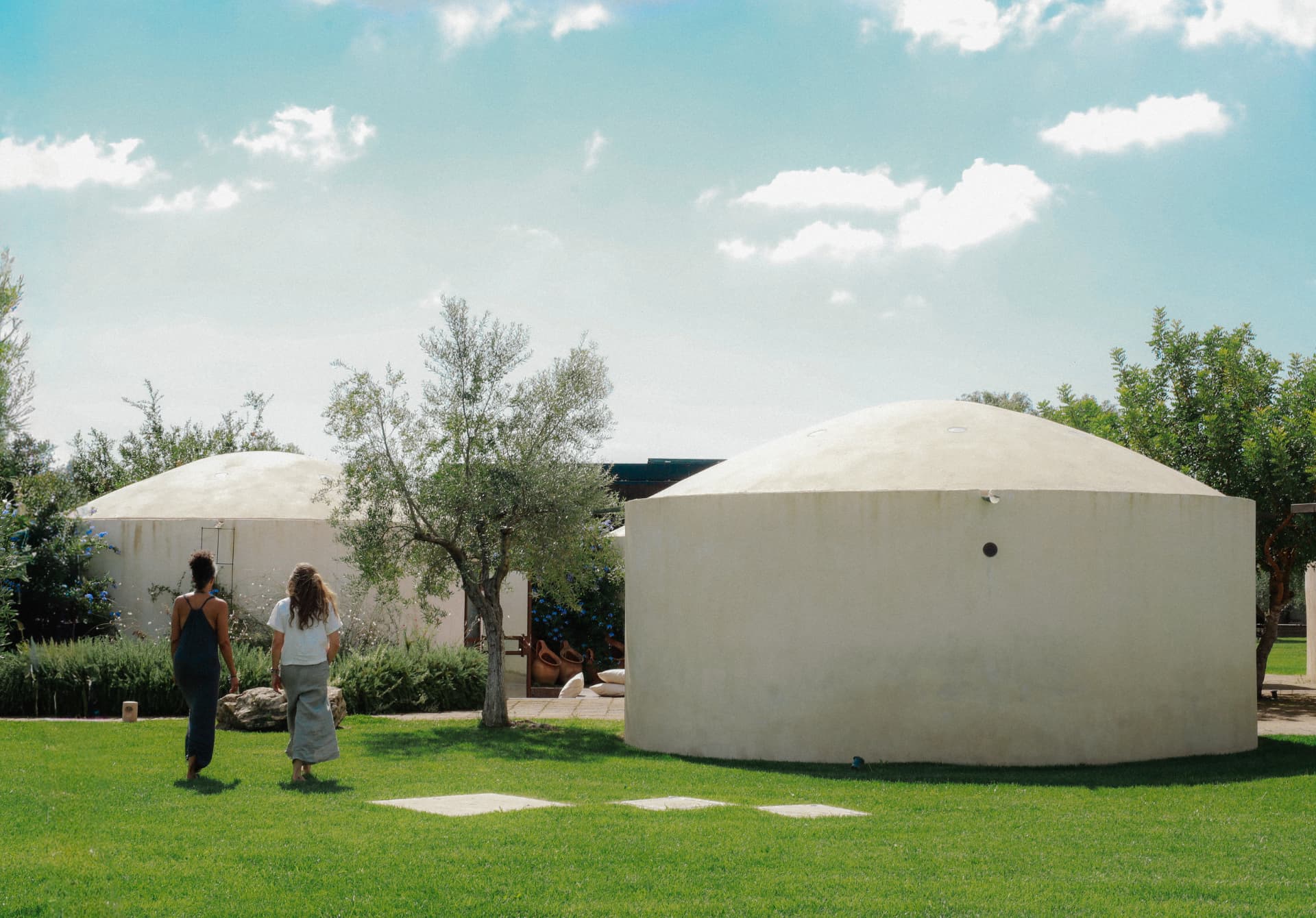 Round white accommodation buildings on a green lawn beneath a bright sky
