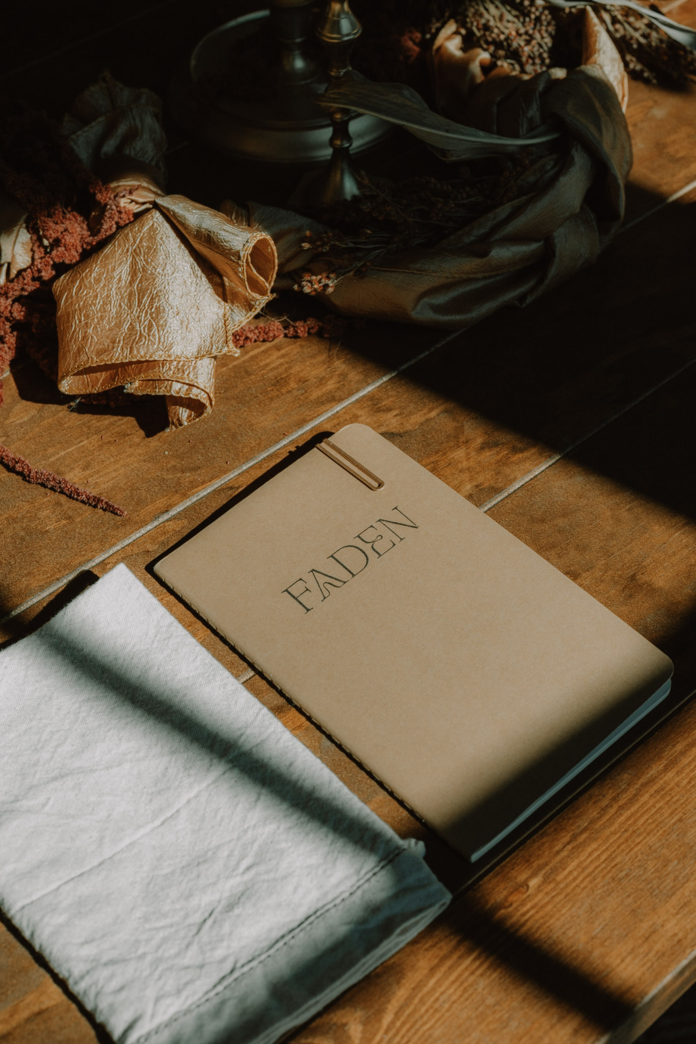 A FADEN notebook resting beside linen and botanical objects on a sunlit wooden table