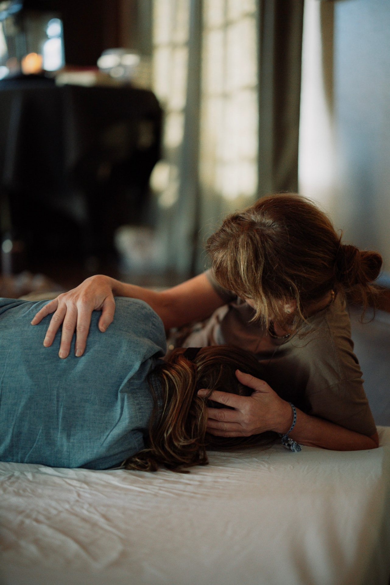 A woman gently holding another woman’s head as she rests on a white mattress