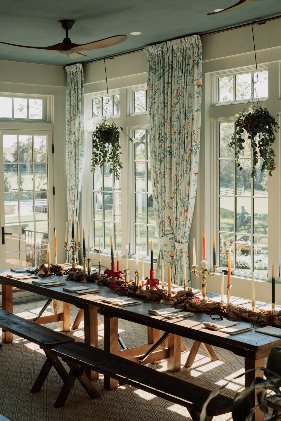 A sunlit dining room with floral curtains and a long candlelit table