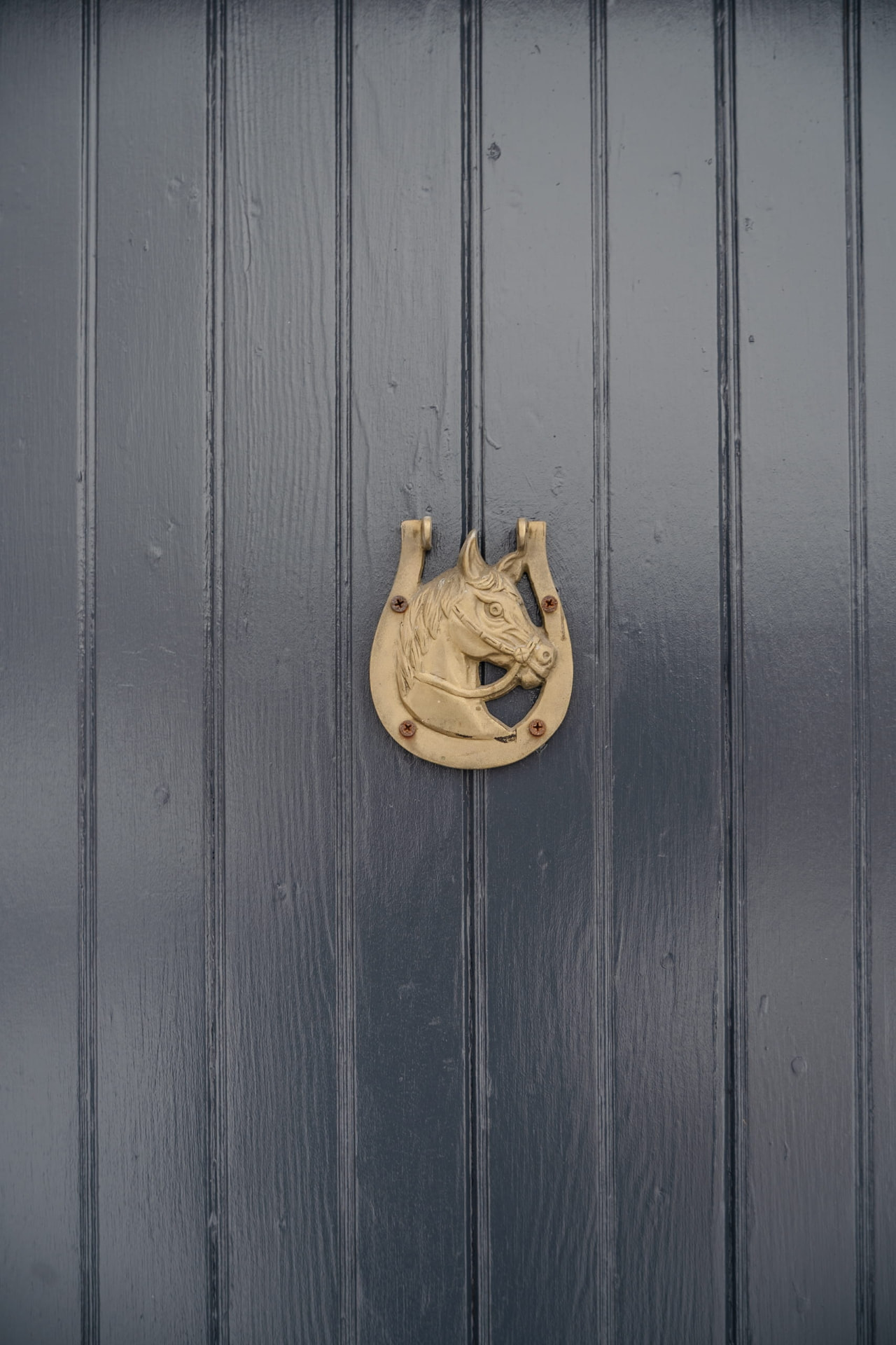 A brass horse and horseshoe door knocker on a dark painted cottage door