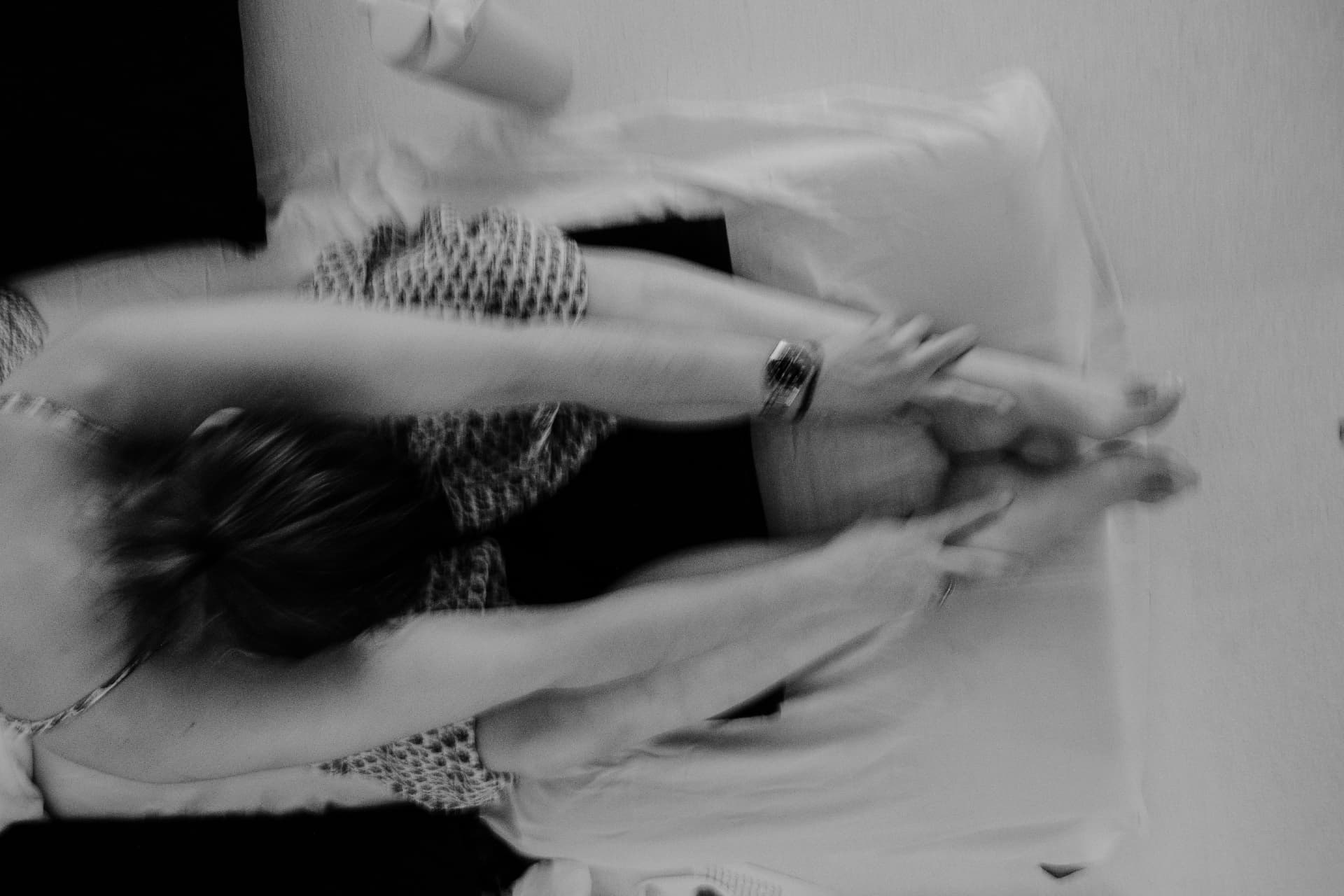 A softly blurred woman stretching her arms as another rests nearby, in black and white