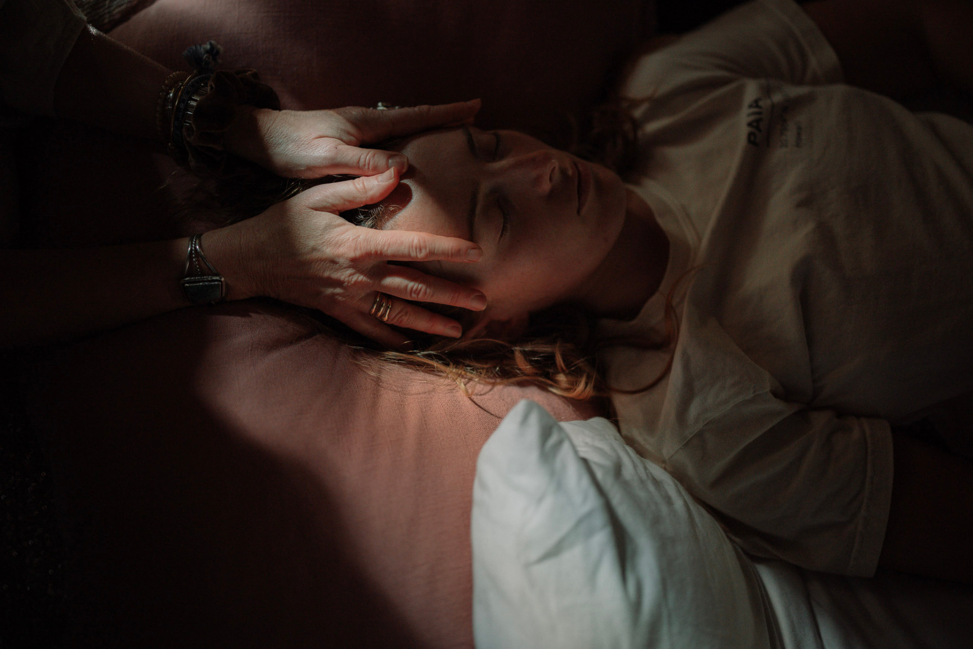 Hands gently resting around the temples of a woman lying on a cushion