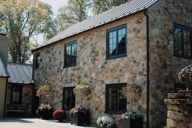A stone farmhouse with dark windows and autumn pumpkins at its doorway