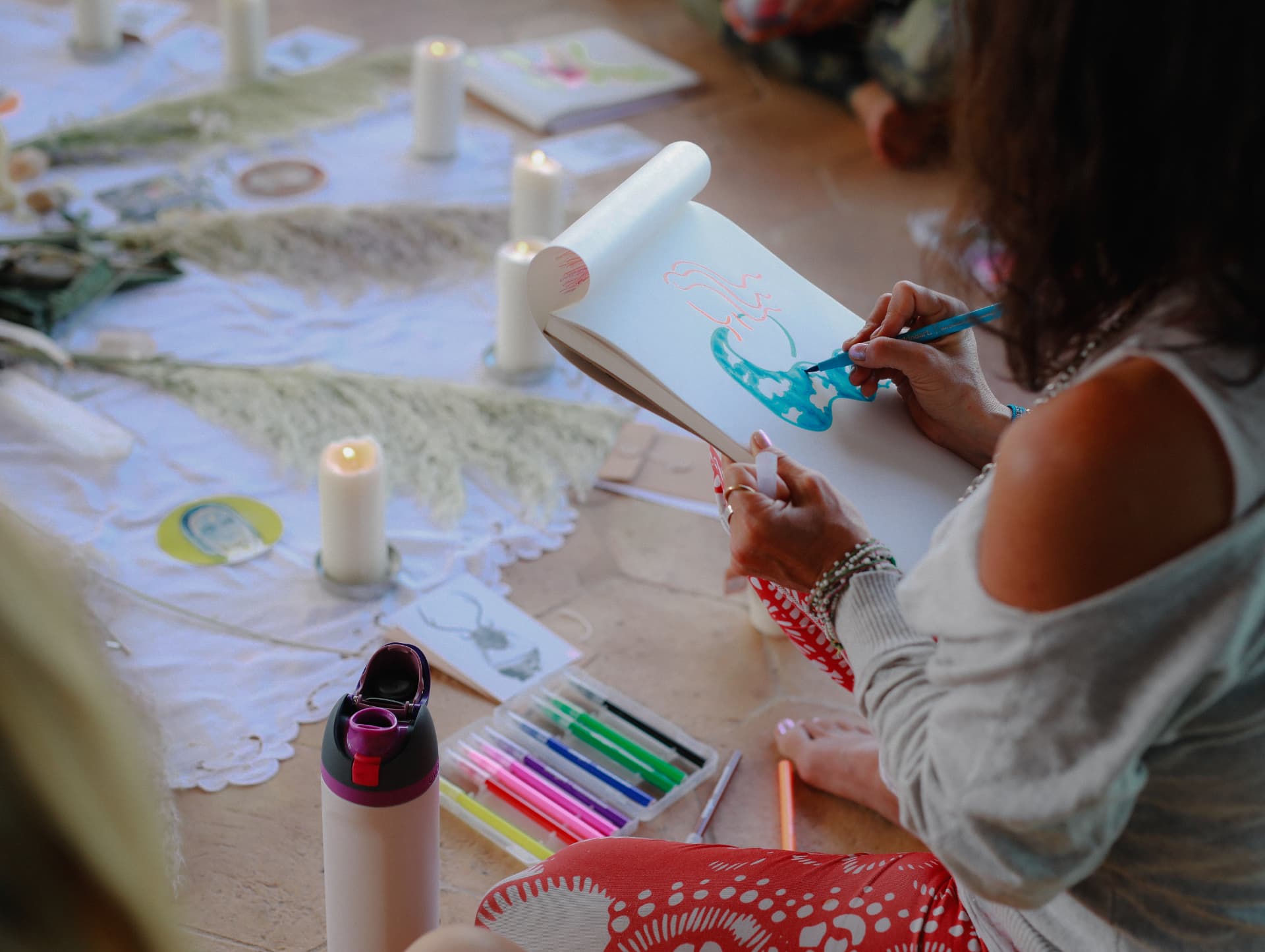 A woman drawing in a sketchbook with blue ink beside candles